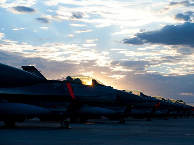 The sun sets behind a row of F-16 Fighting Falcons during Red Flag 14-3, July 16, 2014, at Nellis Air Force Base, Nev. Red Flag provides a series of intense air-to-air combat scenarios for aircrew and ground personnel, which will in turn increase their combat readiness and effectiveness for future real-world missions. In addition to daytime operations, Red Flag conducts training exercises during hours of darkness to train for low visibility environments. (U.S. Air Force photo by Airman 1st Class Thomas Spangler)