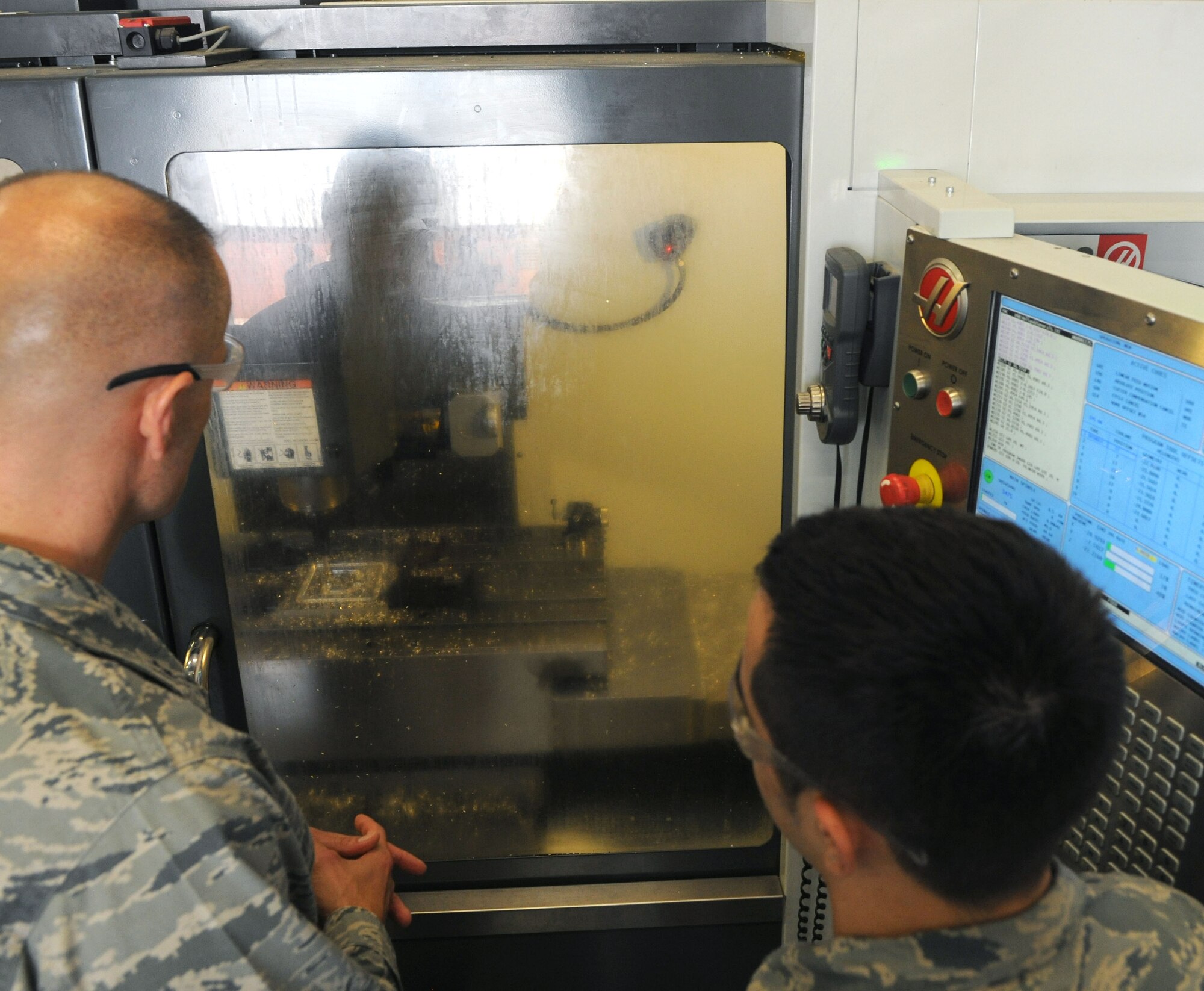 U.S. Air Force Senior Airman Steven McElyea, right, 100th Maintenance Squadron Aircraft Metals Technology journeyman from Lake Whitney, Texas, teaches U.S. Air Force Brig. Gen. Bradley Spacy, U.S. Air Forces in Europe and Air Forces Africa director of logistics, installations and mission support, how to use a computer numerical control milling machine in the 100th MXS during a visit July 25, 2014, to RAF Mildenhall England. McElyea taught Spacy how to start, run and complete a product on the milling machine to demonstrate how quickly and properly aircraft parts can be made if necessary. (U.S. Air Force photo/Senior Airman Kate Maurer/Released)