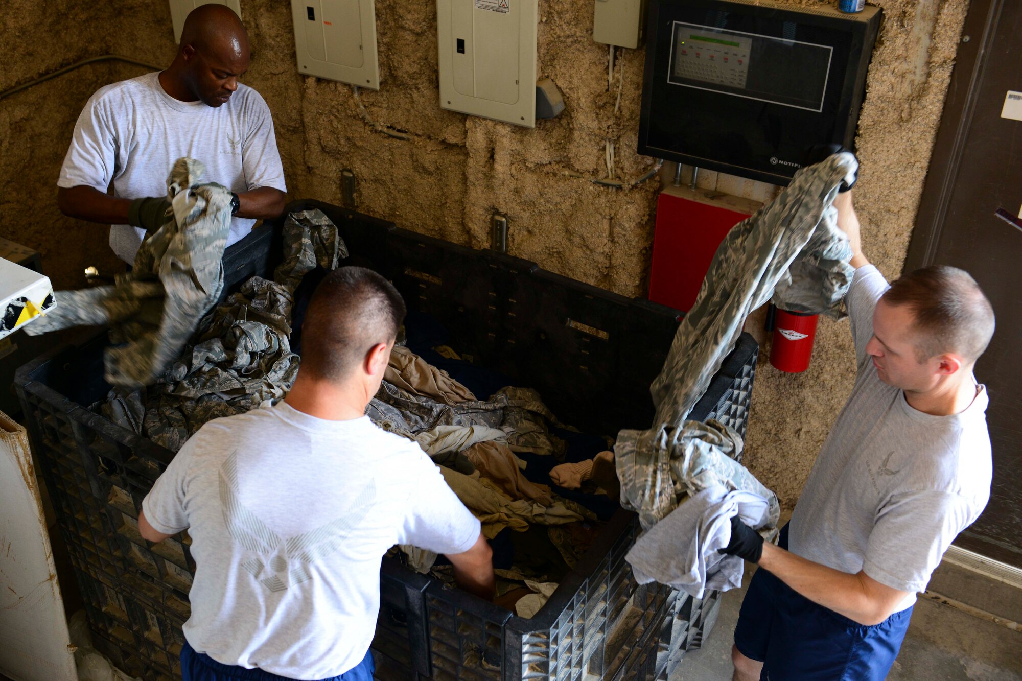 U.S. Air Force Airmen assigned to the 379th Expeditionary Security Forces Squadron antiterrorism office, sort through discarded uniforms at Al Udeid Air Base, Qatar, July 24, 2014. AUAB has 15 drop off boxes, where unwanted, worn and unserviceable uniform items can be discarded.  (U.S. Air Force photo by Staff Sgt. Ciara Wymbs)