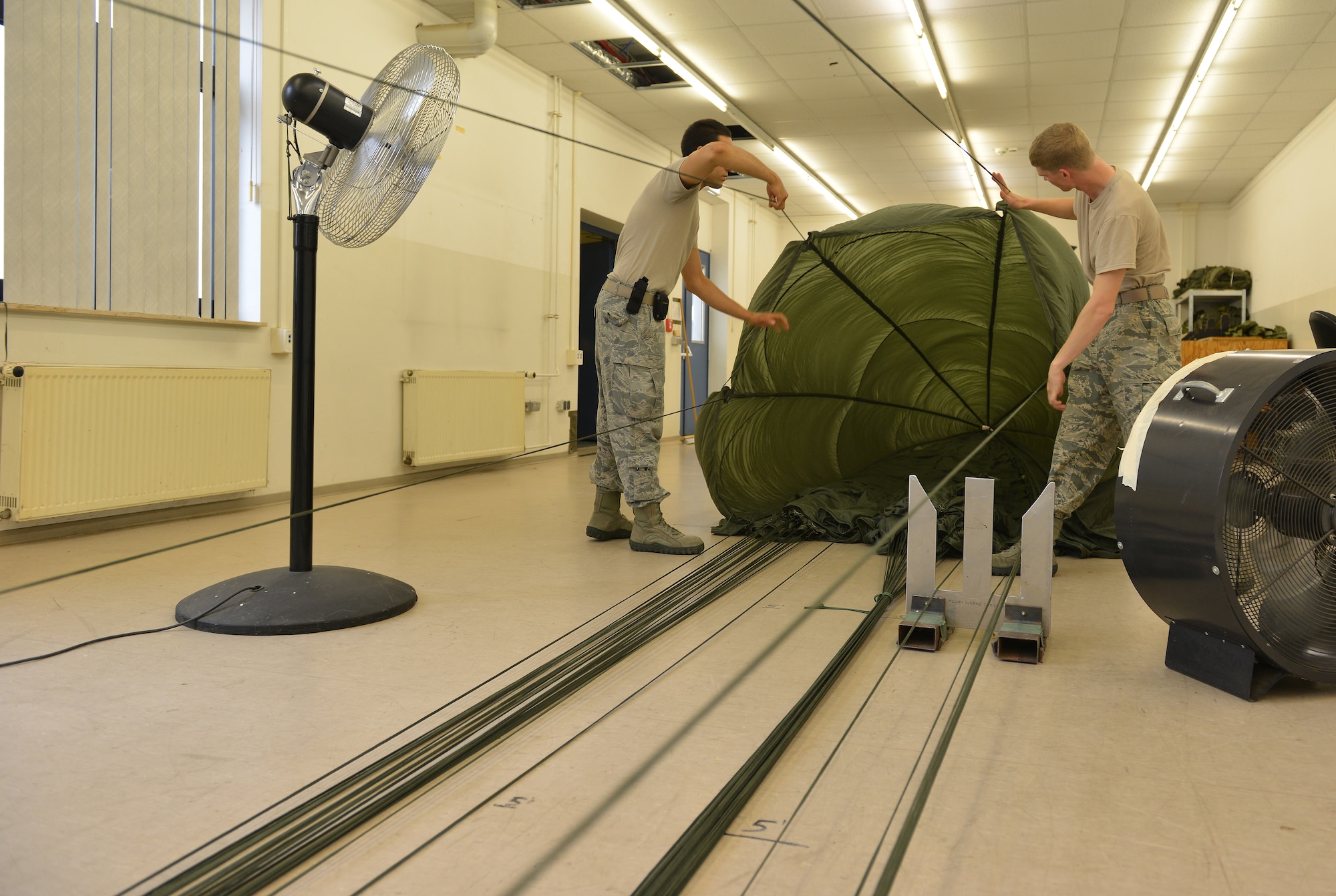 Senior Airman Brian Rodriguez and Airman 1st Class Kyle Taylor, 86th Logistics Readiness Squadron aerial delivery specialists, inspect a cargo parachute before it gets folded, July 23, 2014, Ramstein Air Base, Germany. Airmen of the aerial delivery department prepare different types of cargo parachutes and goods for air drops support missions around the world. (U.S. Air Force photo/Senior Airman Holly Mansfield)
