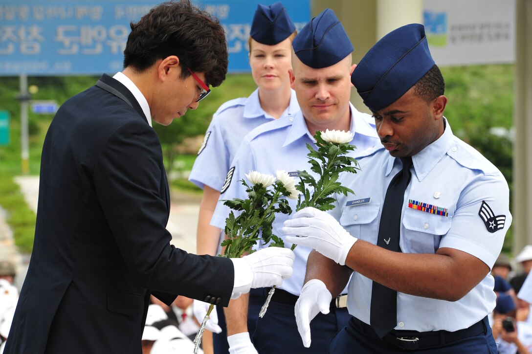 Senior Airman Rodrick Chandler (front), 8th Medical Operations Squadron dental technician, accepts a white chrysanthemum to be placed ceremoniously during an Armistice Agreement anniversary ceremony, while Tech. Sgt. Luke Coleman (middle), 8th Aircraft Maintenance Squadron, 35th Aircraft Maintenance Unit support section chief, and Tech. Sgt. Chelsea Hughes, 8th Operations Support Squadron NCO in charge of targets intelligence, follow suit at Imsil National Cemetery, Republic of Korea, July 22, 2014. The three were part of a detail of five Airmen who represented the groups and wing staff agencies of the 8th Fighter Wing during the event. (U.S. Air Force photo by 1st Lt. Earon Brown/Released)