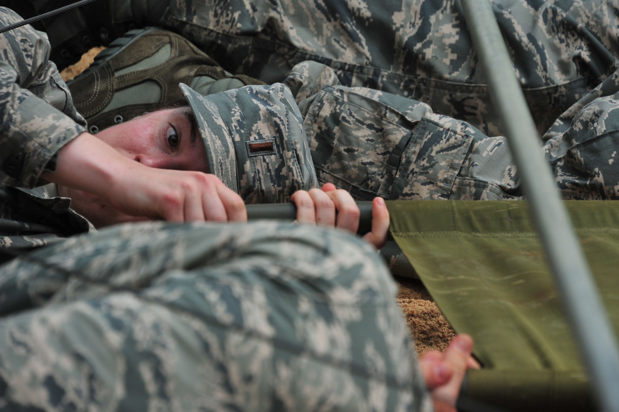 MAXWELL AIR FORCE BASE, Ala. -- A Commissioned Officer Training School student helps fellow students move a gurney while under simulated fire at an Officer Training School exercise complex here July 24, 2014. The trainee’s team had to low-crawl to avoid the simulated fire. Commissioned medical, legal and chaplain officers must go through COT to receive military leadership training. This obstacle was a part of a deployment exercise, which tests leadership decision-making as well as contingency operations knowledge. (U.S. Air Force photo by Staff Sgt. Natasha Stannard)