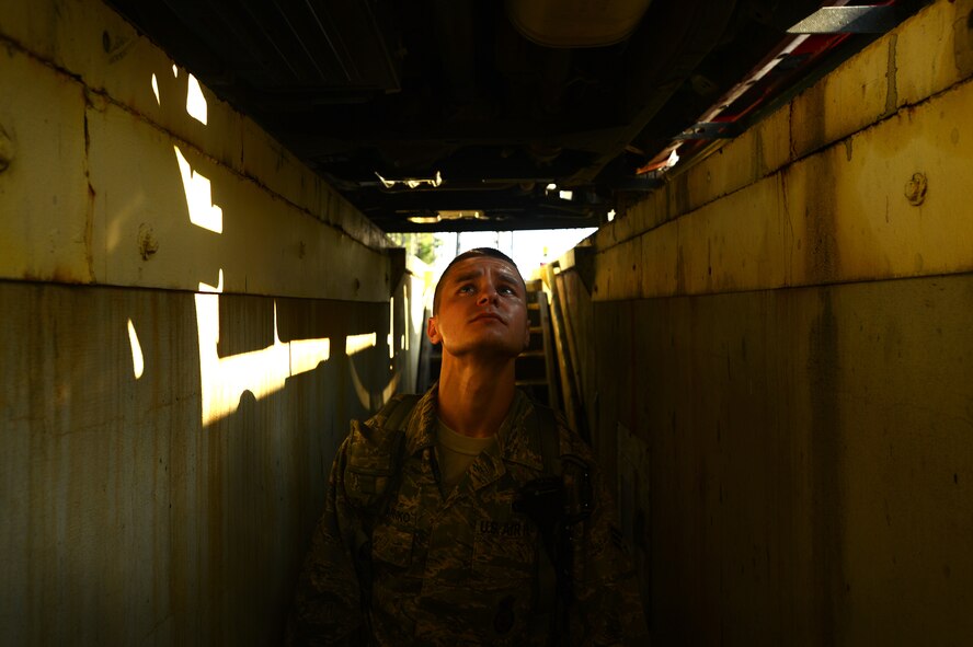 U.S. Air Force Senior Airman Ilya Makarenko, 20th Security Forces Squadron installation entry control journeyman, looks underneath a vehicle at the commercial vehicle inspection area at Shaw Air Force Base, S.C., July 24, 2014. On some vehicles, instead of inspection mirrors, 20th SFS Airmen use a below ground walkway to better view the undercarriage. (U.S. Air Force photo by Airman 1st Class Jensen Stidham/Released)