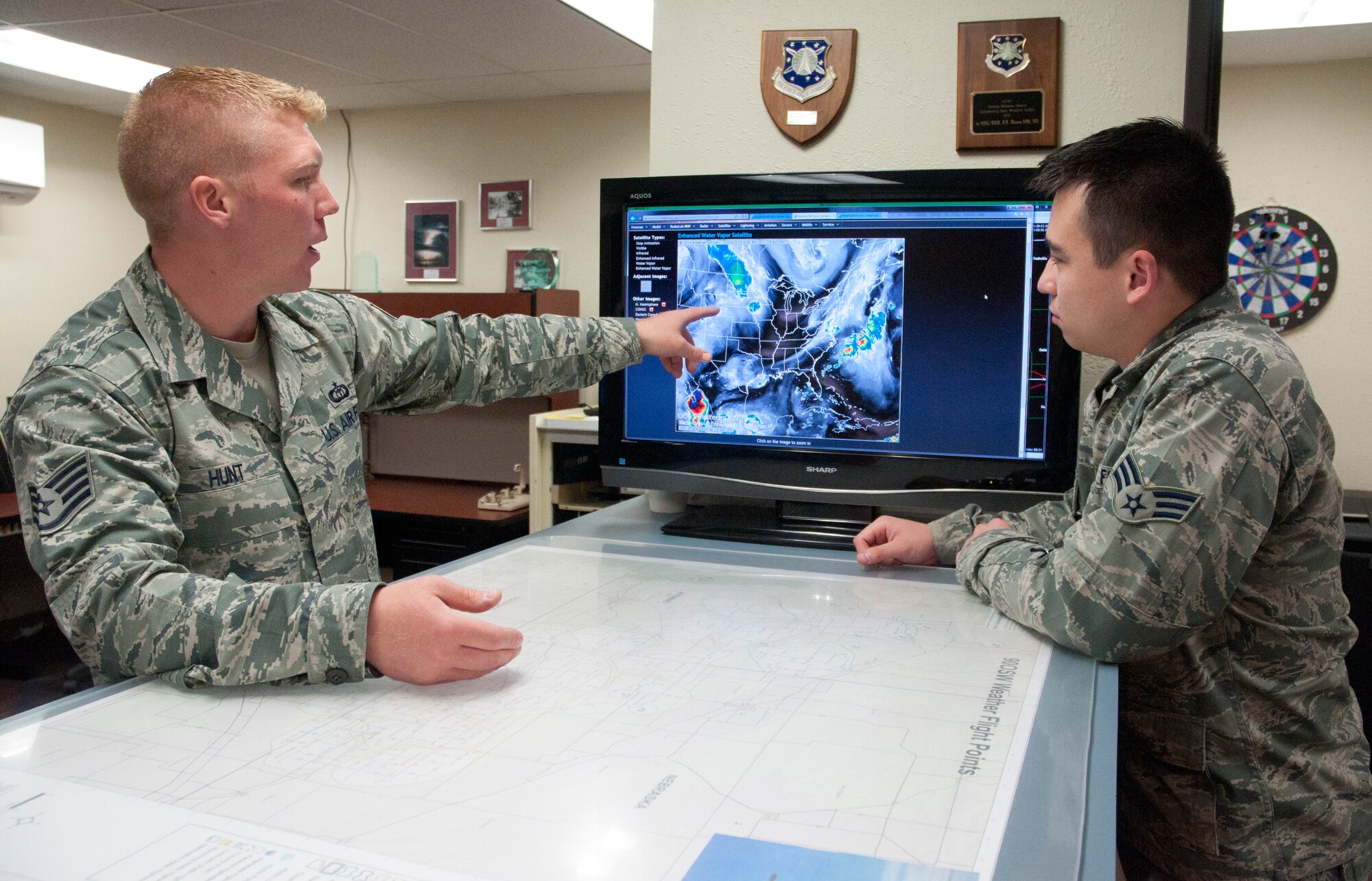 Staff Sgt. Ryan Hunt, 90th Operations Support Squadron, discusses weather patterns with Senior Airman Nelson, 90th OSS, in the weather office July 24, 2014. The weather office has a multitude of resources at their disposal to provide weather forecasts to support base operations. (U.S. Air Force photo by Airman Malcolm Mayfield)