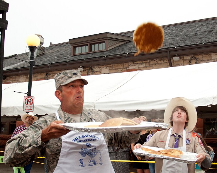 Col. Trevor Flint, 90th Maintenance Group commander, zeroes in on a flying pancake in Depot Plaza, Cheyenne, Wyo., July 23, 2014 while a local scout waits for another to come down. Free pancake breakfasts, feeding thousands of visitors, are a tradition during the annual Cheyenne Frontier Day festivities, with local organizations volunteering to handle the spatulas and tossing the flapjacks to other volunteers waiting to catch them. (U.S. Air Force photo by R.J. Oriez)