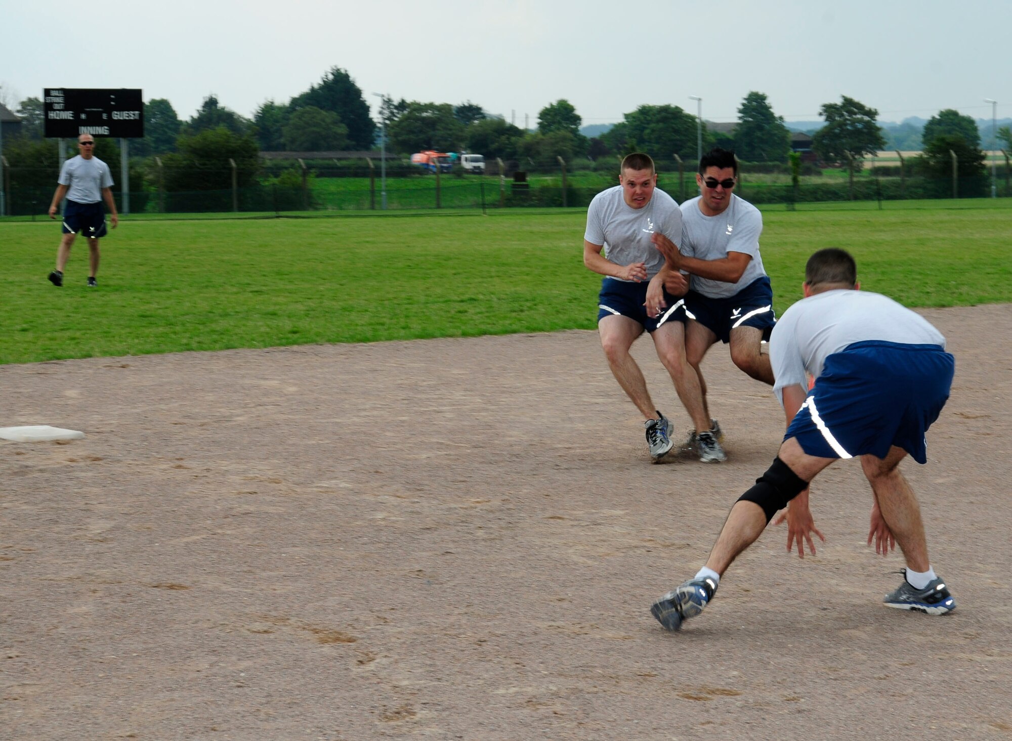 U.S. Air Force Staff Sgt. Troy Pittman, second from left, 100th Maintenance Squadron isochronal inspection aerospace craftsman from Mahomet, Ill., blocks the running path of U.S. Air Force Senior Airman Ernesto Riojas, 100th Aircraft Maintenance Squadron propulsion technician from Laredo, Texas, as he makes his way from second to third base during a game of kickball at the 100th Maintenance Group sports day July 21, 2014, on RAF Mildenhall, England. The 100th MXG Airmen and families participated in various sports events, which were followed by a barbecue to build morale within the group and foster a family environment. (U.S. Air Force photo/Karen Abeyasekere/Released)