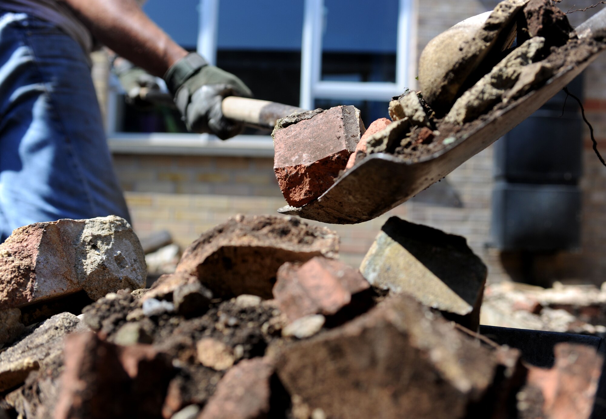 U.S. Air Force Tech. Sgt. David West, 100th Civil Engineer Squadron emergency management NCO in charge from Columbia, S.C., shovels broken brick into a wheelbarrow from a courtyard garden during a renovation project July 26, 2014, at Beck Row Primary School in Beck Row, Suffolk, England. Volunteer Airmen from the 100th CES removed most of two brick flower beds to make room for a sensory garden and saved all of the reusable soil and bricks for other future projects. (U.S. Air Force photo/Senior Airman Kate Maurer/Released)