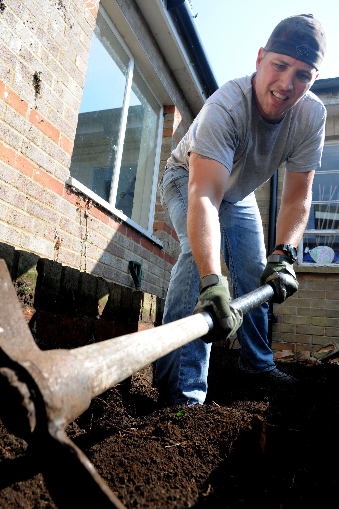 U.S. Air Force Tech. Sgt. David West, 100th Civil Engineer Squadron emergency management NCO in charge from Columbia, S.C., uses a pickaxe to remove brick from a courtyard garden during a renovation project July 26, 2014, at Beck Row Primary School in Beck Row, Suffolk, England. Volunteer Airmen from the 100th CES removed most of two brick flower beds and will continue to spend time renovating the courtyard into a more accessible and cost-effective sensory garden for the students. (U.S. Air Force photo/Senior Airman Kate Maurer/Released)