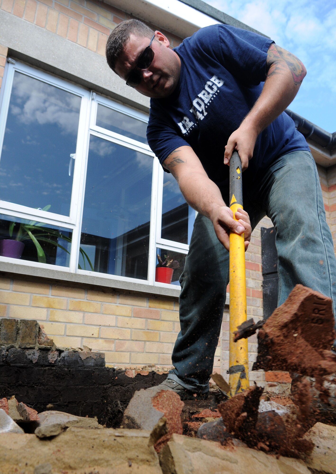 U.S. Air Force Staff Sgt. Geoffry Wadsworth, 100th Civil Engineer Squadron emergency manager from Westborough, Mass.,  removes brick from a courtyard garden with a sledge hammer during a renovation project July 26, 2014, at Beck Row Primary School in Beck Row, Suffolk, England. Volunteer Airmen from the 100th CES removed most of two brick flower beds and will continue to spend time renovating the courtyard into a more accessible and cost-effective sensory garden for the students. (U.S. Air Force photo/Senior Airman Kate Maurer/Released)