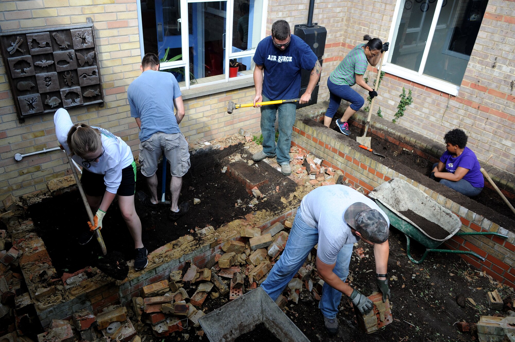 Volunteer Airmen from the 100th Civil Engineer Squadron remove brick and dirt from a courtyard garden during a renovation project July 26, 2014, at Beck Row Primary School in Beck Row, Suffolk, England. The courtyard contained two flower beds that were difficult to maintain. It will eventually house a more accessible and cost-effective sensory garden for the students. (U.S. Air Force photo/Senior Airman Kate Maurer/Released)