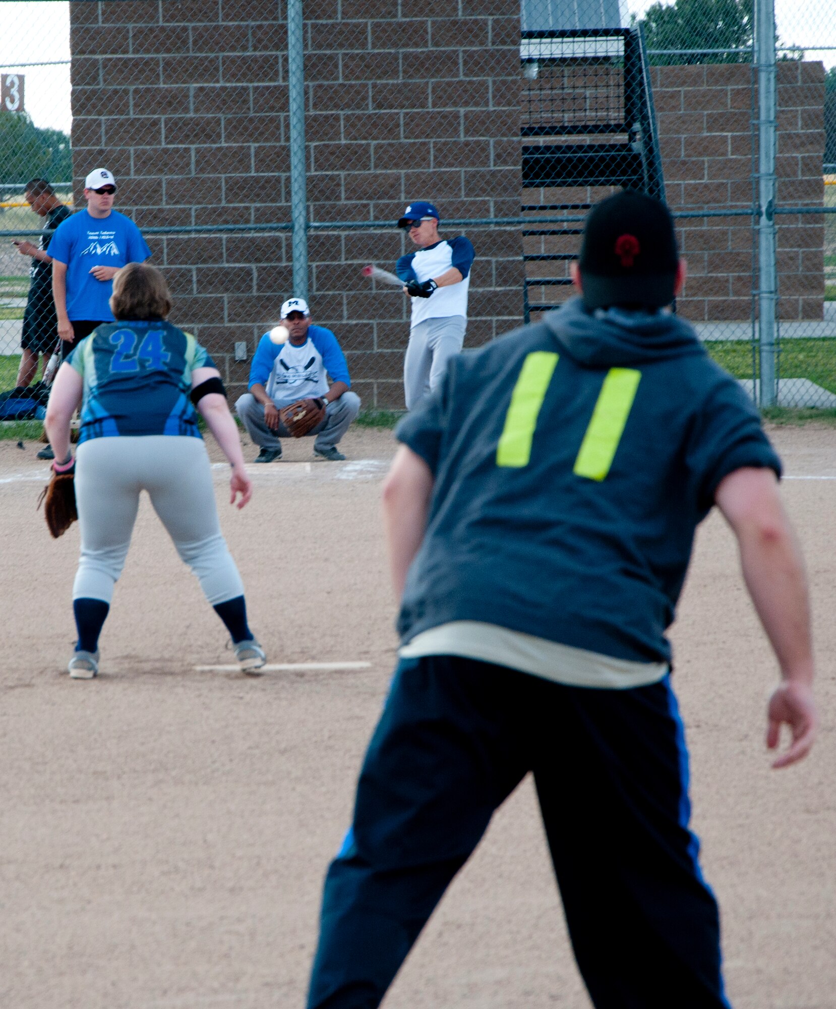 Calvin Wong, 90th Munitions Squadron, connects with the softball pitched by Briana Tinsley, 90th Missile Security Forces Squadron, during the intramural softball game between the 90th MUNS and the 90th MSFS July 28, 2014, on one of the F.E. Warren Air Force Base, Wyo., softball fields. Chris Butkowski (foreground), 90th Logistics Readiness Squadron supply liaison to the 90th MUNS and 90th MUNS softball team player, waits to see if the drive will be caught before gunning for third base. (U.S. Air Force photo by Airman 1st Class Jason Wiese)