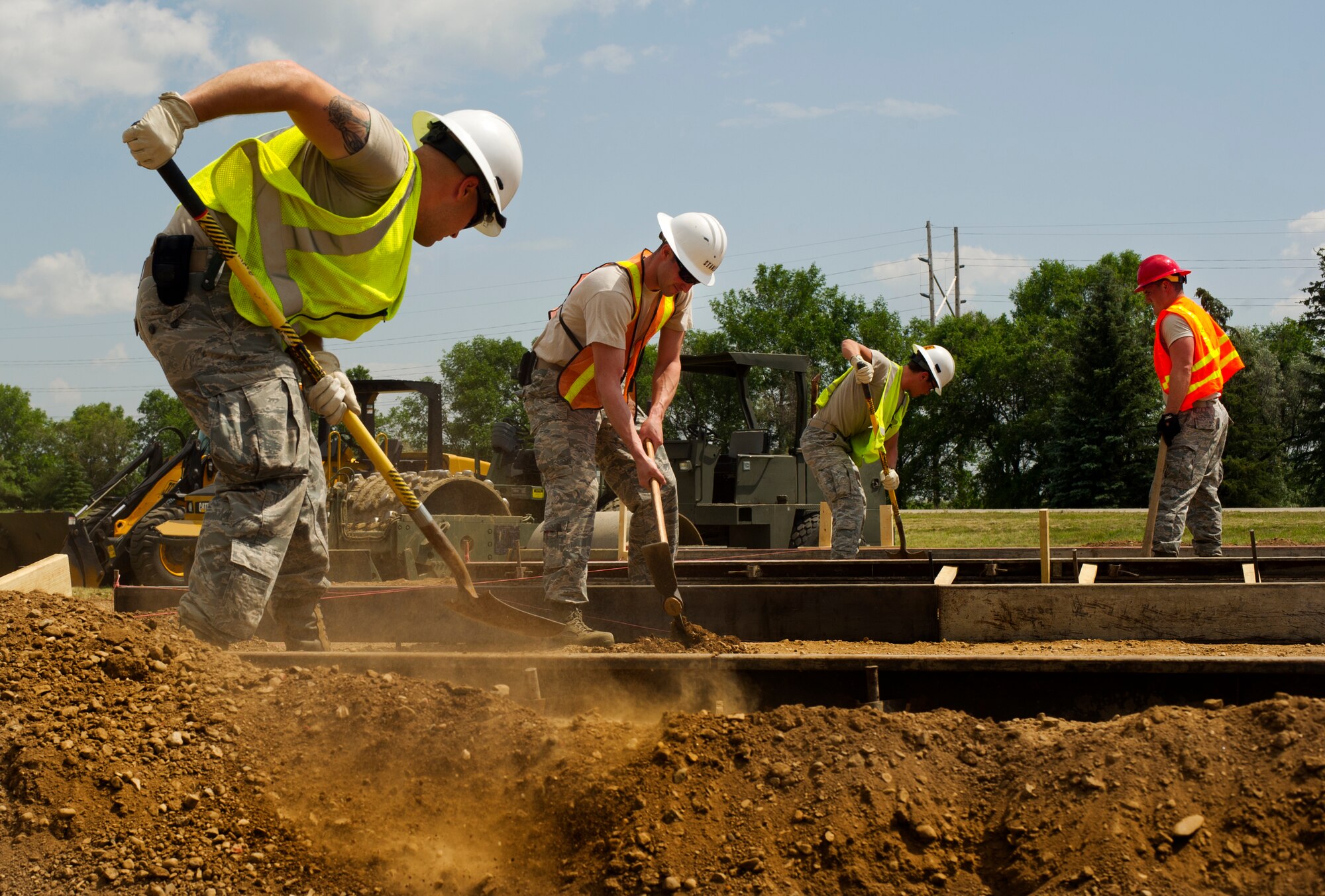 Airmen from the 5th Civil Engineer Squadron use picks and shovels to loosen and dig up dirt during construction of a new search facility on Minot Air Force Base, N.D., July 15, 2014. There are approximately 60 Airmen from eight different Air Force specialty codes within the 5th CES involved in this project. (U.S. Air Force photo/Senior Airman Brittany Y. Bateman)