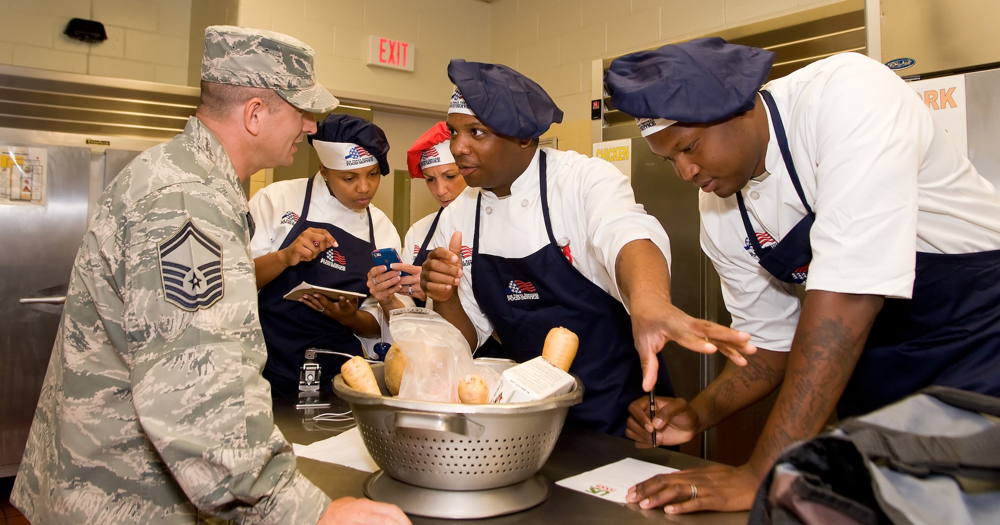 Staff Sgt. Earl Simmons, second from right, 315th FSS, Joint Base Charleston, S.C., discusses their menu plan with Senior Master Sgt. Brian Denny, left, Air Force Mortuary Affairs Operations port mortuary superintendent, during the Dover Iron Chef competition July 24, 2014, at the Patterson Dining Facility on Dover Air Force Base, Del. Simmons and three other members on the AFMAO team had two and a half hours to prepare, cook and present their appetizer, entrée and dessert to a panel of three judges. (U.S. Air Force photo/Roland Balik)
