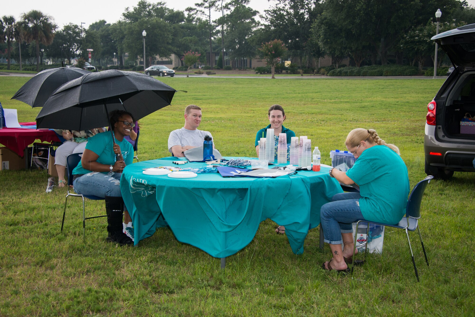 Representatives of Keesler's Sexual Assault Prevention and Response office huddle under umbrellas during a block party July 25, 2014, next to the Shaw House, Keesler Air Force Base, Miss.  The event, hosted by the Airman's Council and the Dorm Council, was open to all ranks and benefitted the 81st Training Wing Airmen recognition fund. (U.S. Air Force photo by Marie Floyd)