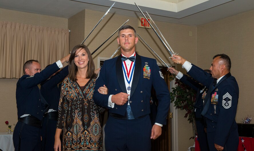 U.S. Air Force Master Sgt. Corey Hebb, 820th Combat Operations Squadron NCO in charge of innovative combat equipment, escorts his wife Fallin through a saber detail during a senior NCO induction ceremony at Moody Air Force Base, Ga., July 25, 2014. Each member of the saber detail represented the senior enlisted tier. (U.S. Air Force photo by Airman 1st Class Ceaira Tinsley/Released)
