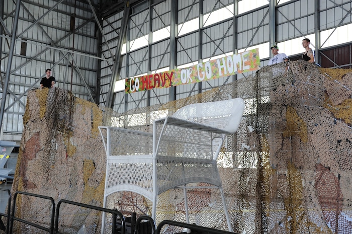 JOINT BASE CHARLESTON, S.C. – (From left to right) Airman 1st Class Matthew Gardner, Tech. Sgt. Brian LeClaire, and Senior Airman Donald Kirby, 2014 Triple Pack Combat Dining Out committee members, raise a banner over an eight-foot tall wicker chair located behind the head table in preparation for the Dining Out ceremony July 26, 2014, at Joint Base Charleston, S.C.  This year marked the first-ever combined event at JB Charleston, involving all three wings — the 628th Air Base Wing and the 437th and 315th Airlift Wings. The theme of this year’s event was “Go heavy or go home,” referring to the heavy airlift capability of the C-17 Globemaster III cargo aircraft stationed at JB Charleston. (U.S. Air Force photo/1st Lt. Christopher Love)