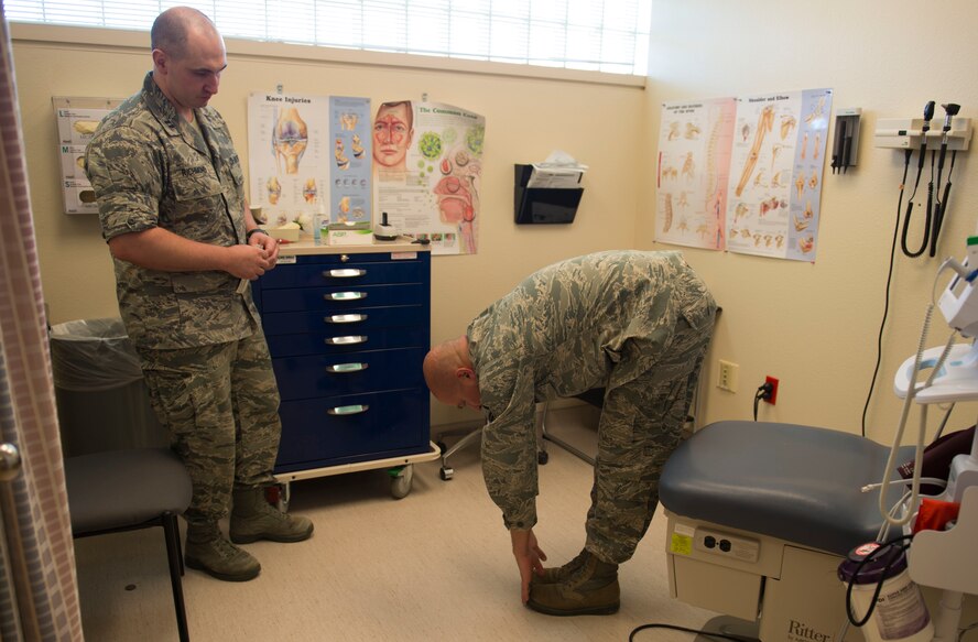 Master Sgt. Nathan Carlson, 219th Security Forces Squadron health technician, touches his toes to locate pain in his back at Minot Air Force Base, N.D., May 22, 2014. Locating and testing pain levels are the first steps in battlefield acupuncture before inserting the studs into the ear. (U.S. Air Force photo/Airman 1st Class Sahara L. Fales)