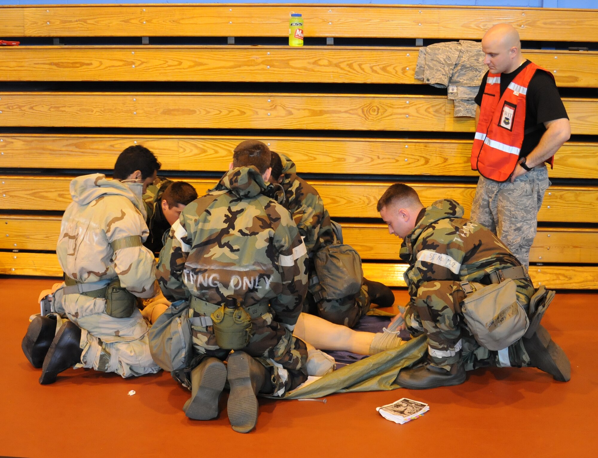 U.S. Air Force Tech. Sgt. Eduardo Clemente, right, 352nd Special Operations Support Squadron independent duty medical technician from Dothan, Ala., observes Airmen simulating self-aid buddy care July 25, 2014, on RAF Mildenhall, England. Airmen learned how to administer first aid while dressed in full personal protective equipment. (U.S. Air Force photo/Gina Randall/Released)