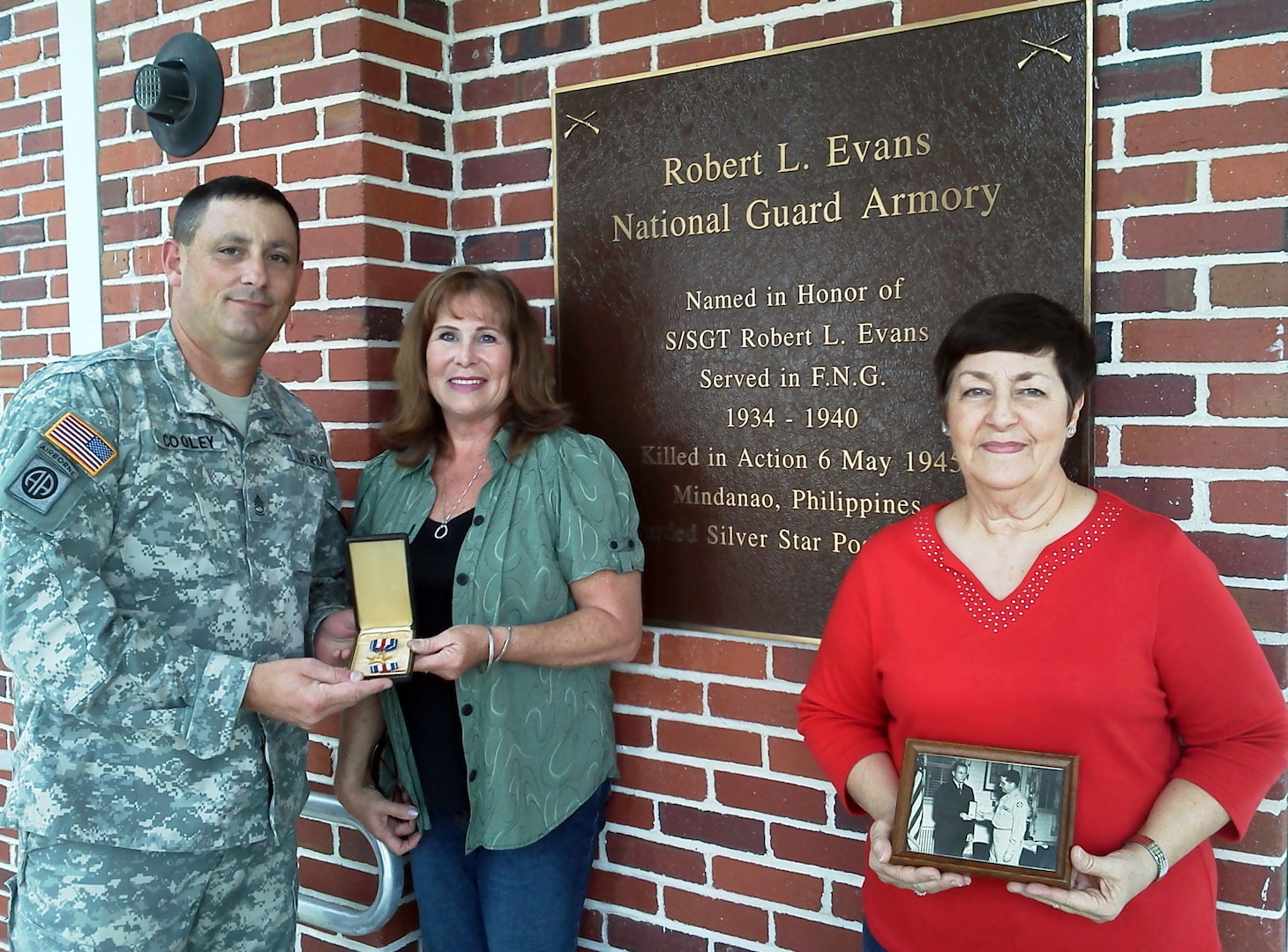 Florida Army National Guard Sgt. 1st Class Carlton Cooley accepts the Silver Star medal of Staff Sgt. Robert Evans from Evans' neices Deborah Lynne Evans Watts (center) and Beverly Evans Srock, at the National Guard Armory in Sanford, Fla., Jan. 10, 2012. Evans, a medic serving with the 124th Infantry Regiment's Medical Detachment, was awarded a posthumous Silver Star after he died in action in the Philippines in 1945. The armory, which was later named after Evans, is now home to B Company, 2nd Battalion, 124th Infantry Regiment. In this photo, Srock is holding a black-and-white photo of Evans' brother Earl receiving the Silver Star for his late brother