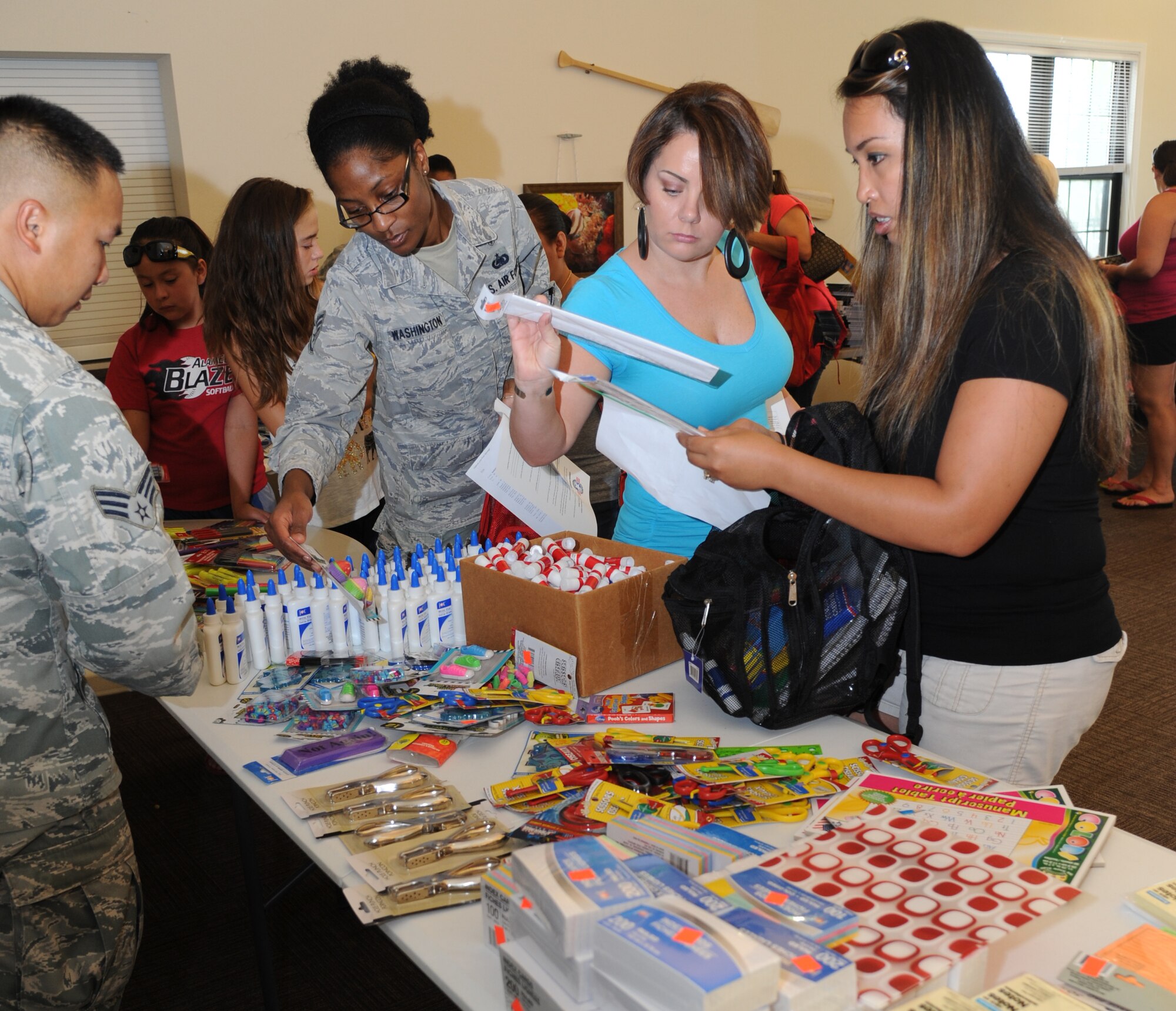 Senior Airman Xeng Xiong, 81st Force Support Squadron, sets out school supplies while Staff Sgt. Sade Washington, 81st Inpatient Operation Squadron; the wife of Navy Petty Officer 2nd Class James Whitehead and the wife of Navy Petty Officer 1st Class Patrick Smith, Naval Construction Battalion Center, Gulfport, Miss., sort through items during a backpack and school supplies give-away event July 29, 2014, at the Bay Ridge Community Center, Keesler Air Force Base, Miss.  The 81st Force Support Squadron and Operation Home Front partnered together to host the event for military families. (U.S. Air Force photo by Kemberly Groue)