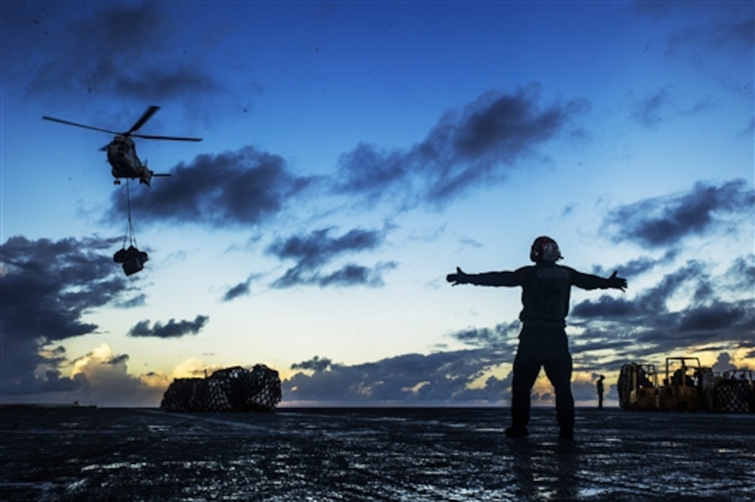 A U.S. Navy sailor aboard the aircraft carrier USS George Washington signals the pilot of an SA330J Puma helicopter as it delivers supplies to the ship's flight deck during a replenishment-at-sea in the Waters East of Okinawa, July 28, 2014. The helicopter crew is assigned to the Military Sealift Command dry cargo and ammunition ship USNS Matthew Perry. 