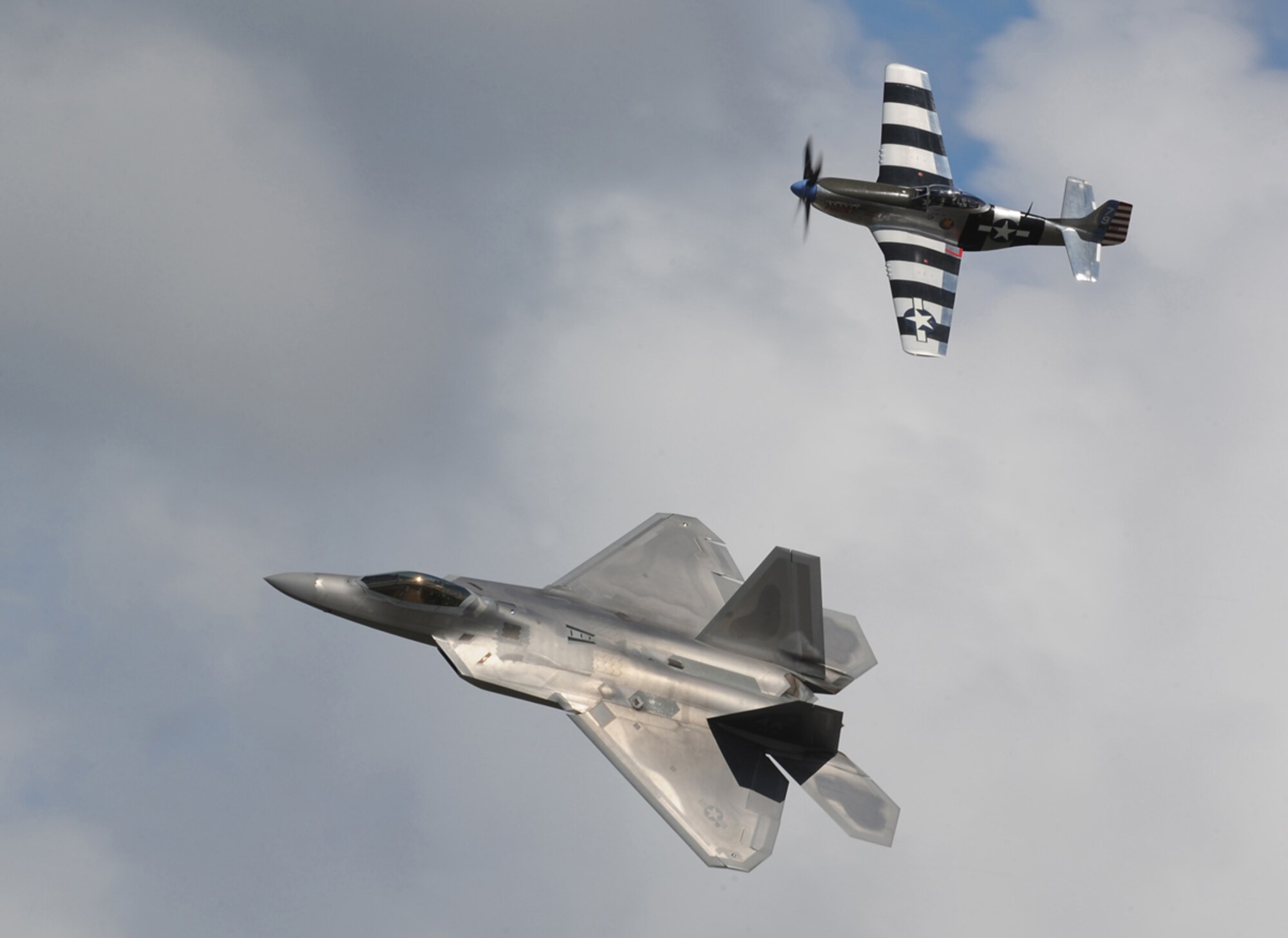 A World War II-era North American P-51 Mustang fighter flies in formation with an F-22 Raptor during the Arctic Thunder Open House biennial event hosted by Joint Base Elmendorf-Richardson, Alaska. The event features more than 40 Air Force, Army and civilian aerial acts, July 25-27, and has an expected crowd of more than 200,000 people. It is the largest two-day event in the state and one of the premier aerial demonstrations in the world. The 2014 Arctic Thunder Open House is a proud part of the Anchorage Centennial Celebration.  (U.S. Air Force photo/Justin Connaher)