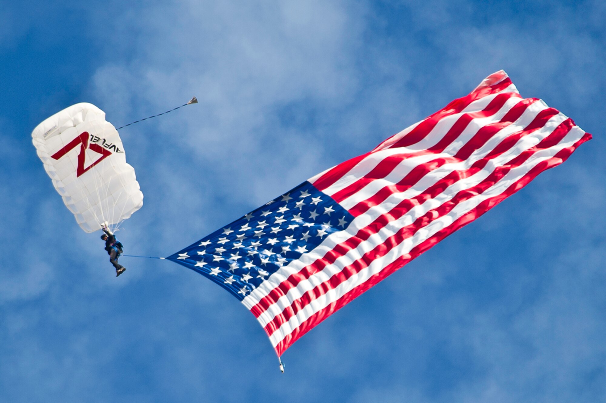 Rex Pemberton parachutist drops from the sky carrying the American flag during the opening ceremony of Arctic Thunder Open House 26, 2014.  Arctic Thunder Open House is a biennial event hosted by Joint Base Elmendorf-Richardson, Alaska. Featuring more than 40 Air Force, Army and civilian aerial acts and an expected crowd of more than 200,000 people, it is the largest two-day event in the state and one of the premier aerial demonstrations in the world. The 2014 Arctic Thunder Open House is a proud part of the Anchorage Centennial Celebration (U.S. Air Force photo by TSgt. Efren Lopez/Released)
