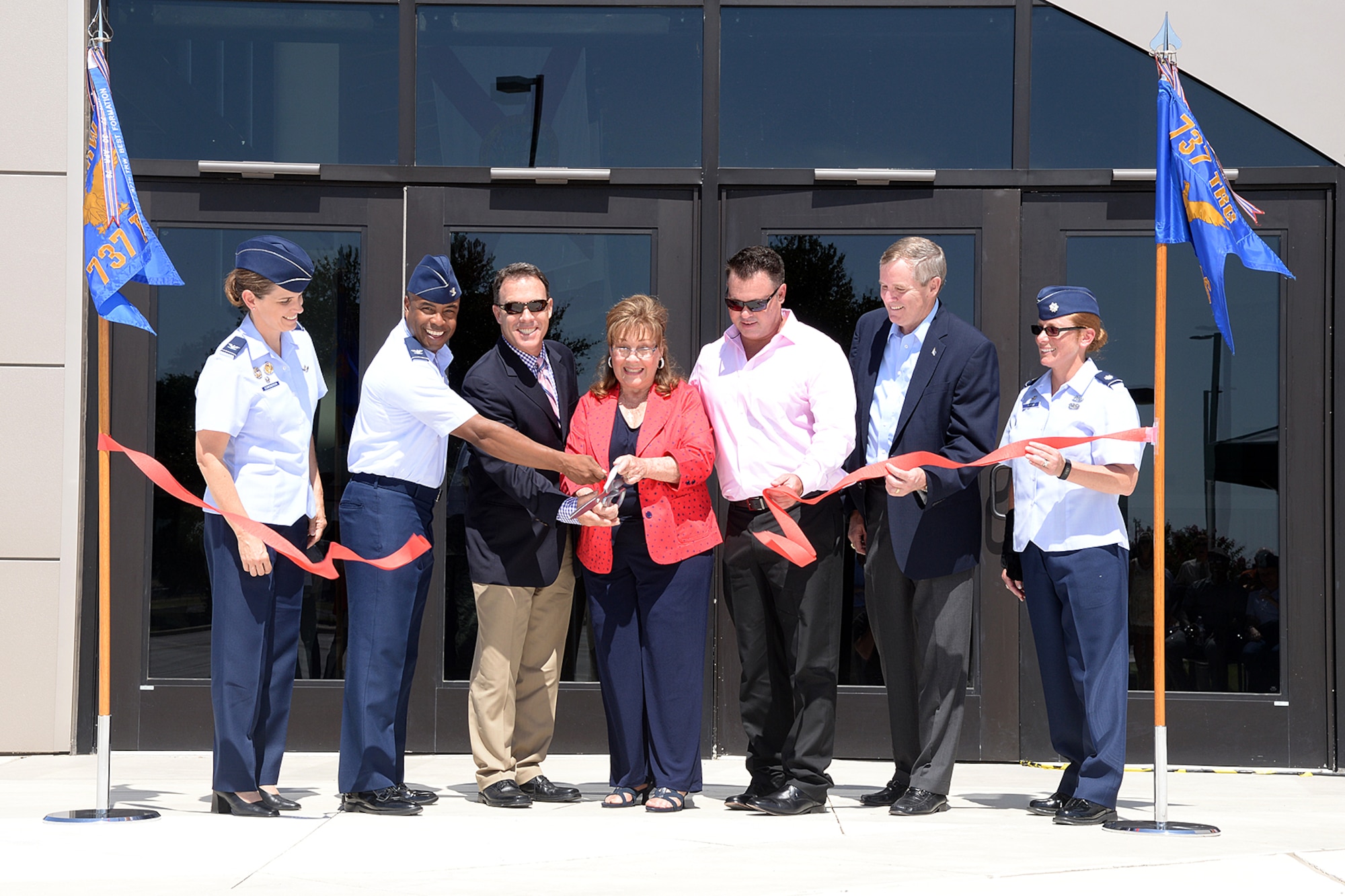 Marsha Pfingston (center) cuts the ribbon to the new Recruit/Family In-processing and Information Center at Joint Base San Antonio-Lackland, Texas July 30, 2014 that was named after her late husband, 10th Chief Master Sergeant of the Air Force Gary Pfingston. Assisting her, from left, were Col. Michele Edmondson, 737th Training Group commander; Col. Trent Edwards, 37th Training Wing commander; her sons, Mark and Brad Pfingston;12th CMSAF Eric Benken; and Lt. Col. Jill Murphy, 737th Training Support Squadron commander. (U.S. Air Force Photo by Benjamin Faske/Released)