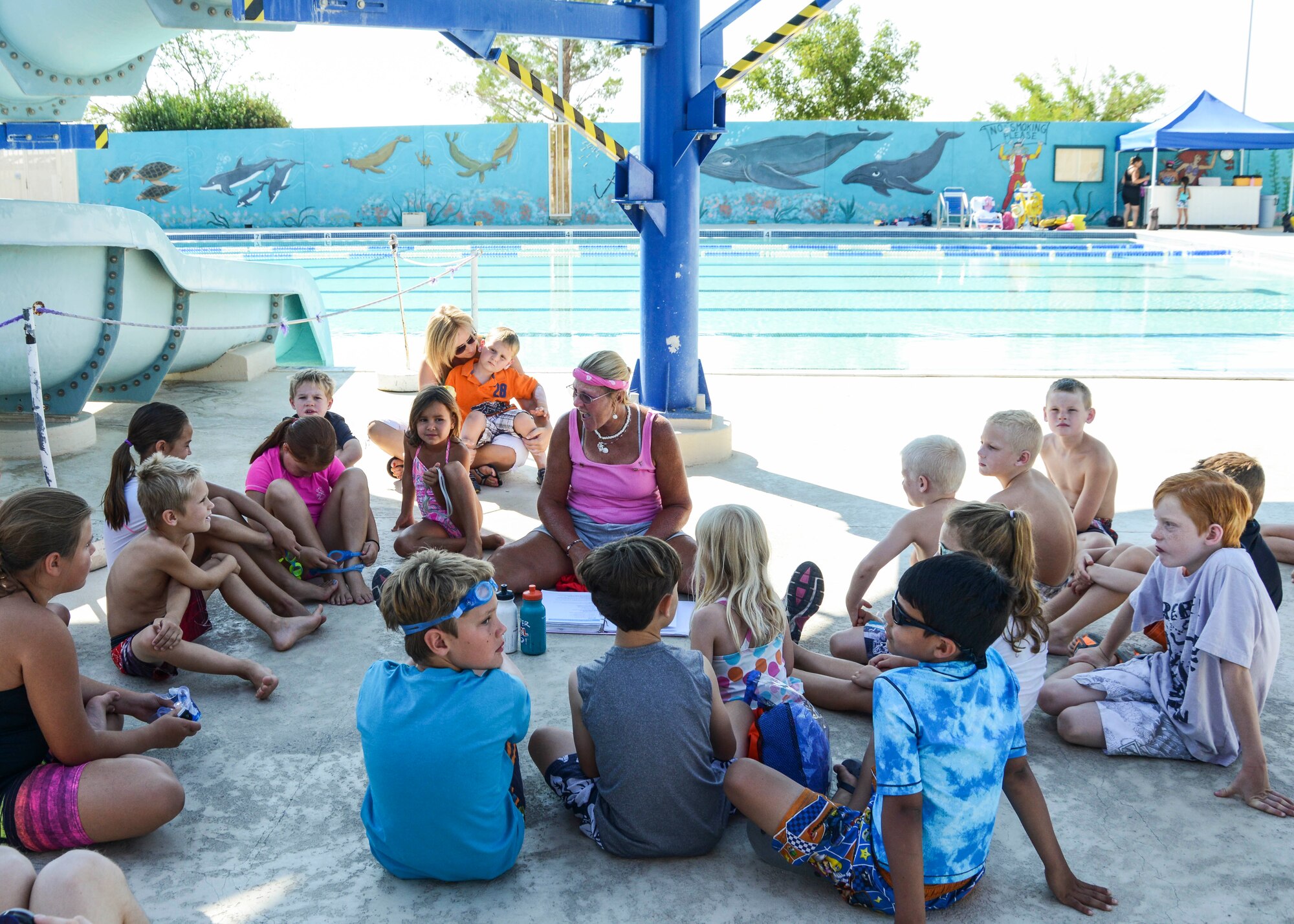Outdoor Recreation's Swim Camp students sit poolside for their daily water safety lessons that teach topics like safety on the deck and pool patrol. The lessons are taught by Sandy Lummer (center), water safety instructor. (U.S, Air Force photo by Rebecca Amber) 