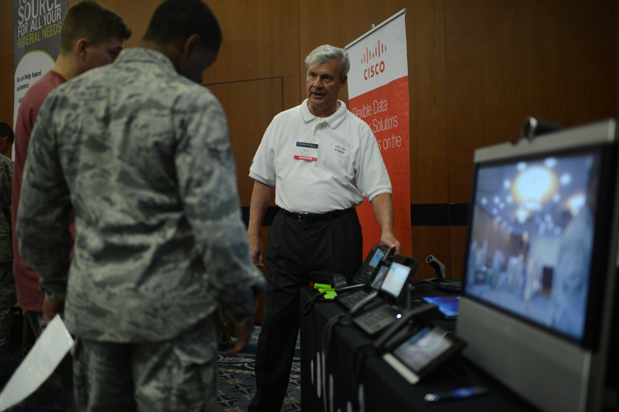 Rick Ottinger, Cisco systems exhibitor, demonstrates new conference-call capabilities at the 2014 Spangdahlem Technology Expo at Club Eifel, July 30, 2014. The display included multiple ways to connect video devices to phone systems for face-to-face real-time interaction. (U.S. Air Force photo by Senior Airman Gustavo Castillo/Released)  