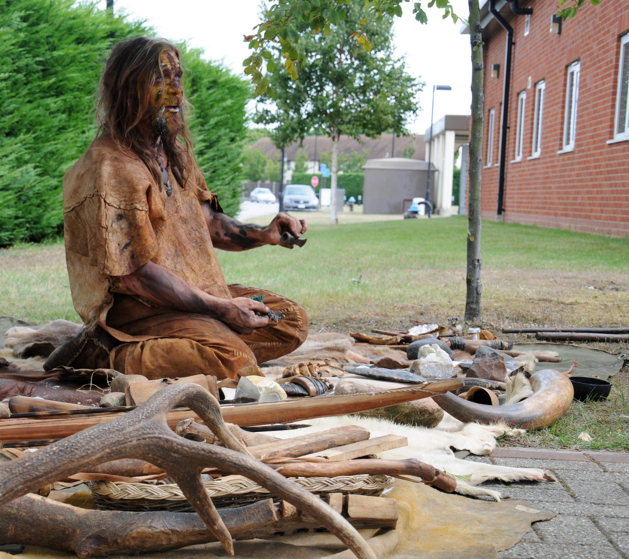 Will Lord, a traditional lifestyle enthusiast from Thetford, Norfolk, demonstrates to Airmen how stone-age people would have dressed and what tools they would have used at the re-opening of the outdoor recreation center July 30, 2014, on RAF Mildenhall, England. Following the official re-opening, guests had the opportunity to look in the new store and talk to staff about the services the center provides. (U.S. Air Force photo/Gina Randall/Released)