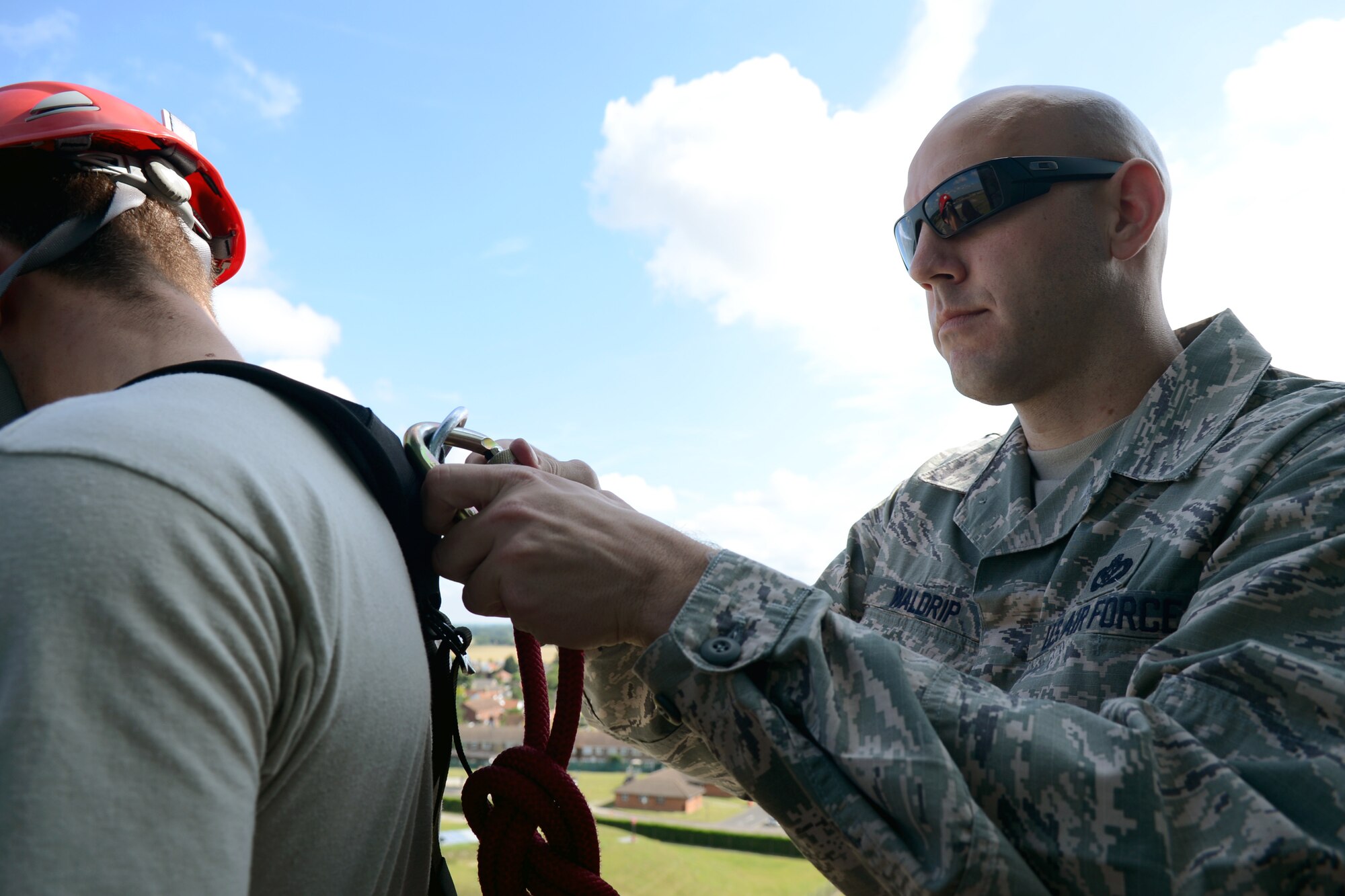U.S. Air Force Master Sgt. Christopher Waldrip, right, 100th Civil Engineer Squadron Fire Department assistant chief of fire prevention from Tuscola, Texas, assists U.S. Air Force Airman 1st Class Brian Adamson, 100th CES Fire Department firefighter from Dearborn, Mich., with attaching the safety line onto his harness July 17, 2014, on RAF Mildenhall, England. Rappelling involves at least two people, one of whom performs the actual rappelling, while the other feeds a safety line down in case the person rappelling begins to fall. (U.S. Air Force photo/Airman 1st Class Kyla Gifford/Released)
