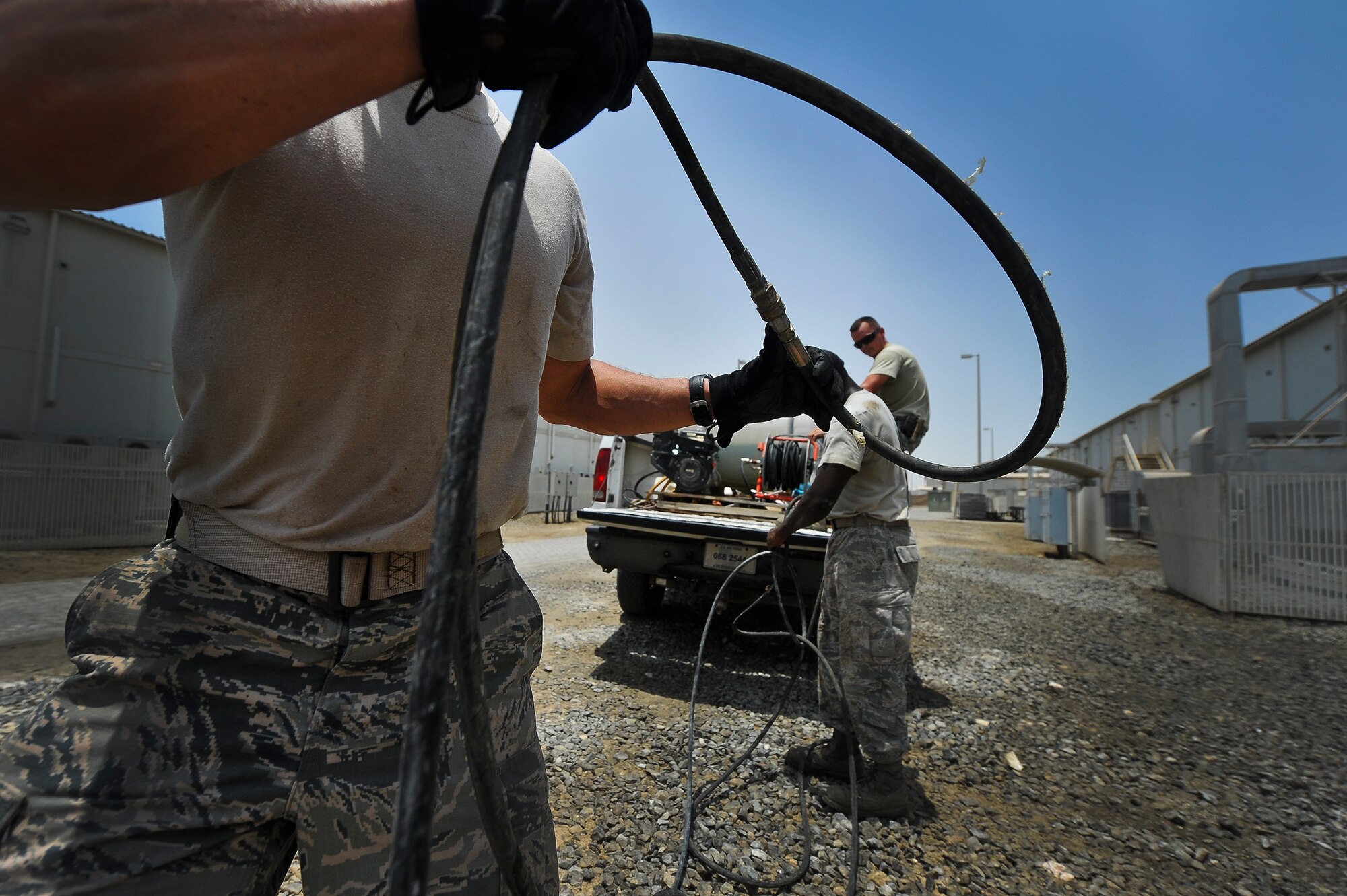 Brig. Gen. John T. Quintas, 380th Air Expeditionary Wing commander, Senior Airman James Jenkins and Staff Sgt. Franklin Sallis, 380th Expeditionary Civil Engineer Squadron heating, ventilation, air conditioning and refrigeration, roll hoses used to clean air conditioning units back into their truck July 28, 2014, at an undisclosed location in Southwest Asia. The job was the chiller team’s last before lunch. Quintas spent the day with the chiller team to gain a better understanding of how Airmen contribute to the mission. (U.S. Air Force photo by Tech. Sgt. Russ Scalf/Released)