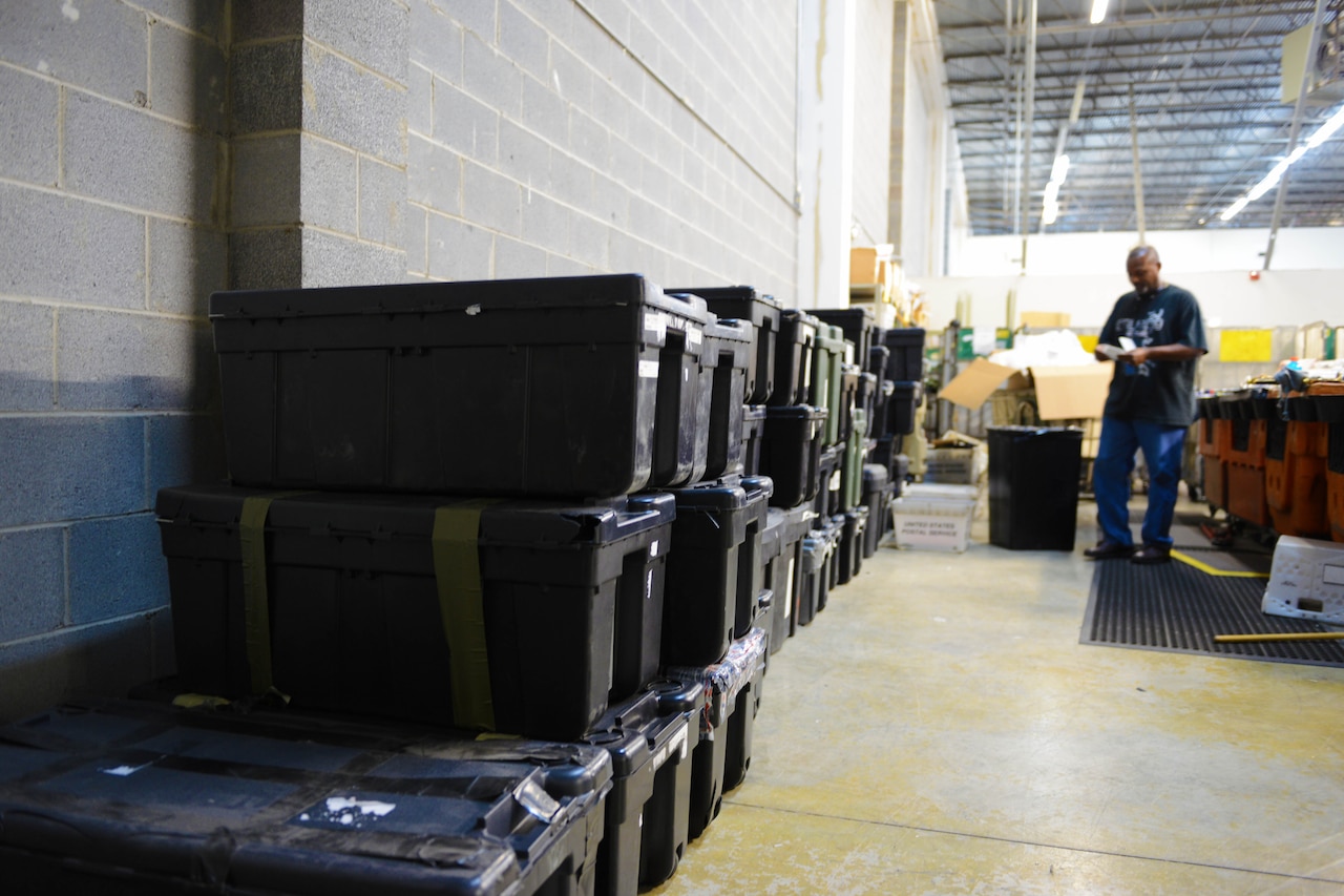 Stacks of lost foot lockers line the walls as Dyrick Fowler, a clerk for the military section of the Mail Recovery Center in Atlanta, the U.S. Postal Service’s only mail recovery center, checks for information to locate service members, July 11, 2014. DoD photo by Army Sgt. 1st Class Tyrone C. Marshall Jr.