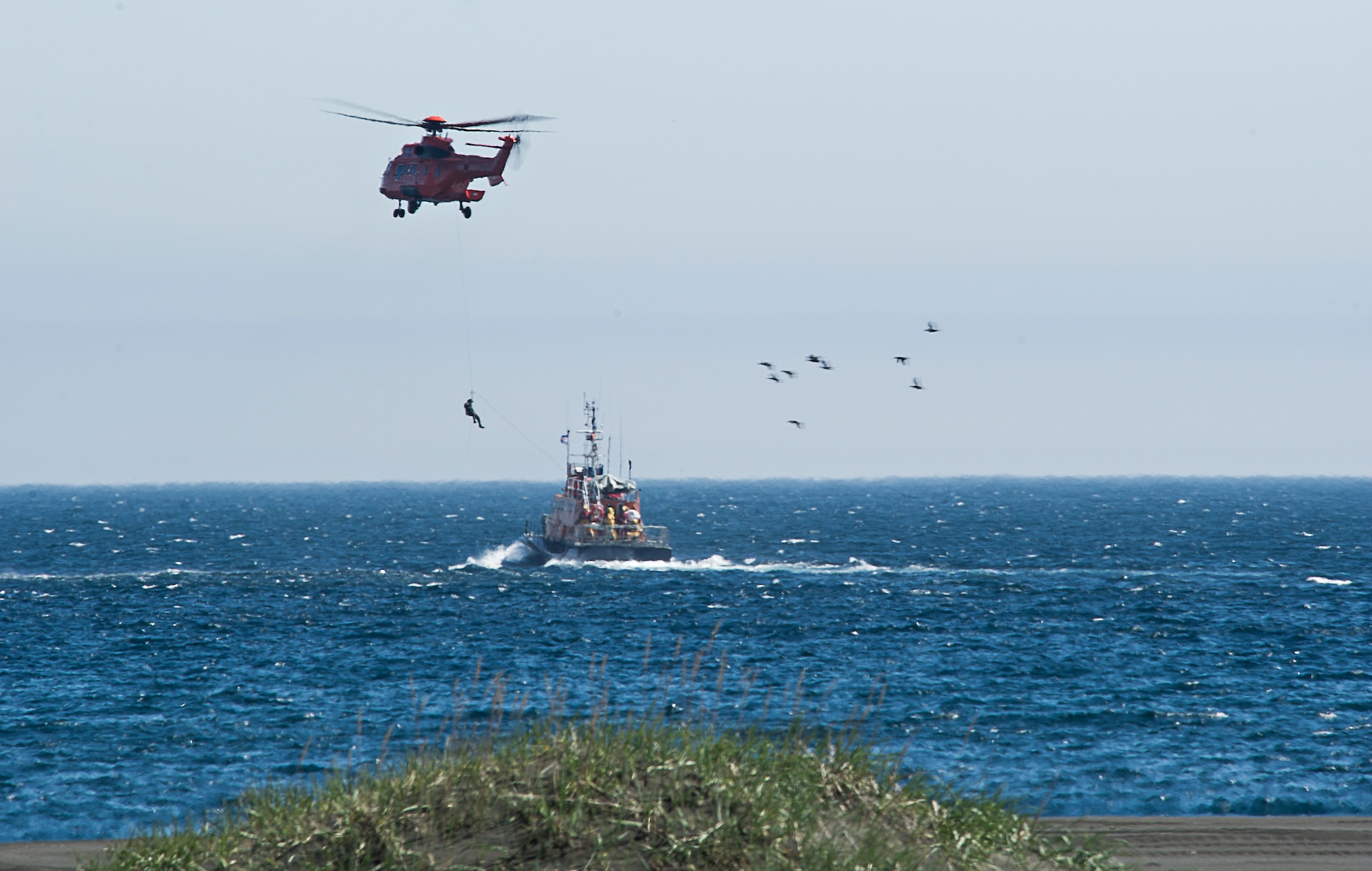 A U.S. Air Force pararescuman descends from an Icelandic Super Puma during a ceremony May 30, 2014, commemorating a rescue mission on the coastline of Voldlavik, Iceland. During the mission, U.S. Airmen saved the lives of six Icelanders stranded aboard their ship, the Godinn. (U.S. Air Force photo/Tech. Sgt. Benjamin Wilson)