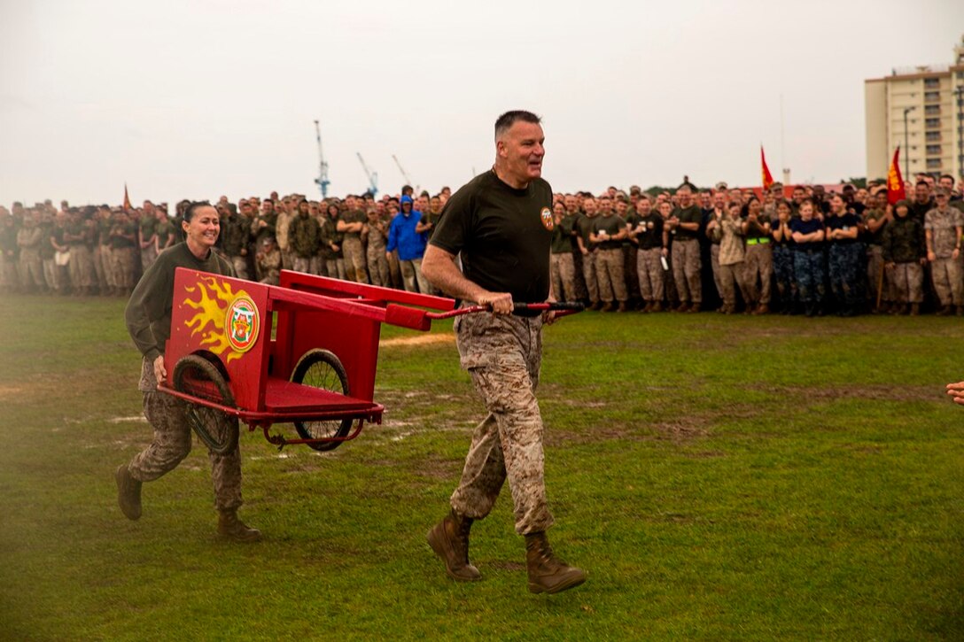 Brig. Gen. Niel E. Nelson, right, and Sgt. Maj. Tamara L. Fode carry their crippled chariot May 23 at Camp Kinser during a field meet. The field meet was in recognition of 3rd Marine Logistics Group’s 56th anniversary. Despite the rainy weather and muddy field, the day’s events included a pancake breakfast, 5-kilometer run, two multi-unit physical training sessions followed by unit competitions. The competitions pitted the most physically fit Marines within the respective battalions and regiments of 3rd MLG against each other in events such as pugil stick bouts, tug-of-war, Humvee pull, tire flip and a functional fitness relay. The culminating event was a sergeant major versus commanding officer chariot race. This year’s winning unit was Combat Logistics Regiment 3, 3rd MLG, III Marine Expeditionary Force. Nelson is the commanding general and Fode is the sergeant major of 3rd MLG, III MEF. 