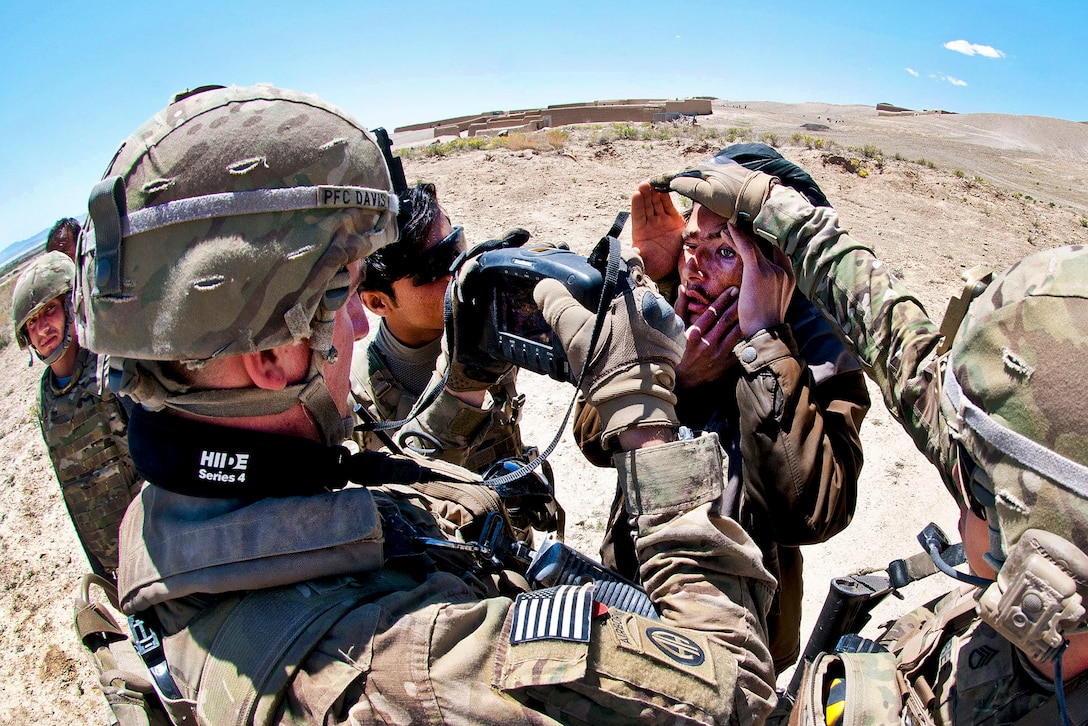 U.S. Army Pfc. Patrick Davis, left, and Staff Sgt. Joshua Tyree, right, shield an Afghan man's eyes from bright sunlight as Davis scans his iris with a handheld identity detection device during a combined clearing operation in Afghanistan's Ghazni province, April 29, 2012. Davis and Tyree are assigned to the 82nd Airborne Division’s 2nd Battalion, 504th Parachute Infantry Regiment, 1st Brigade Combat Team.  
