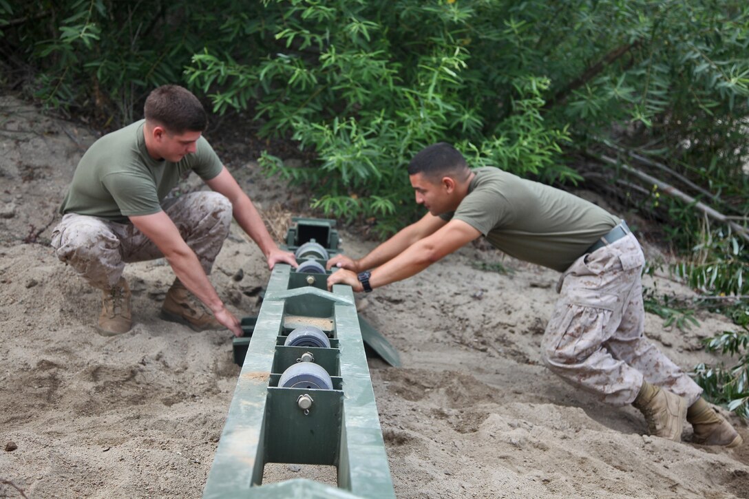 Corporal Jervis Hettrick (left), bridge master, and Lance Cpl. Christopher De Casanova (right), combat engineer, Bridge Platoon, Bridge Company, 7th Engineer Support Battalion, 1st Marine Logistics Group, work together to move a roller beam that will support a bridge, May 29, 2014 for the World Famous Camp Pendleton Mud Run aboard Camp Pendleton, Calif. The annual Mud Run is a 10-kilometer race with several obstacles, which can be negotiated individually or as a team.  This year they built a bridge spanning 71 feet and weighing almost nine tons. On June 6, the Marines who built the bridge plan to participate in Mud Run, as a unit, to increase morale. They will also be volunteering to support the event. (U.S. Marine Corps photo by Lance Cpl. Keenan Zelazoski/ Released)