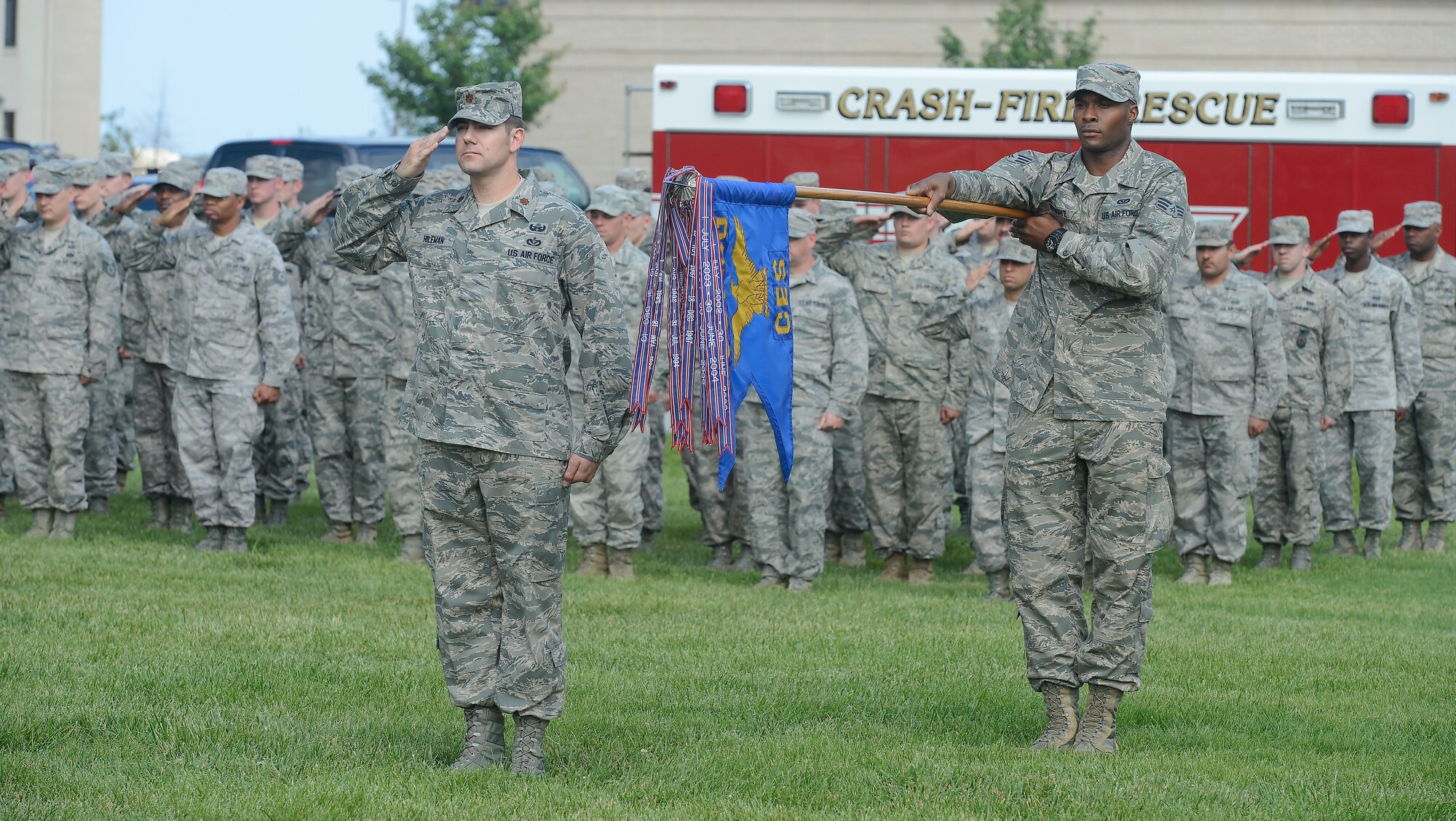 Maj. Matthew Hileman, 436th Civil Engineer Squadron operations flight commander, renders a salute while Senior Airman Andrew Wright, 436th CES electrical shop, presents the unit guidon as the American flag is lowered during a retreat ceremony on May 30, 2014, at Dover Air Force Base, Del. Airman in formation in the background also render salutes.  (U.S. Air Force photo/Greg L. Davis) 