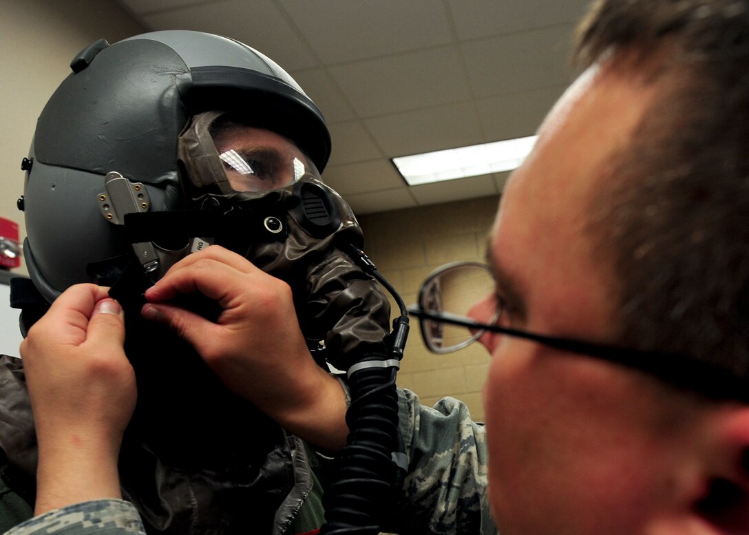 Staff Sgt. William Haller, 28th Operations Support Squadron aircrew flight equipment technician, straps on headgear for Capt. Christopher Ross, 34th Bomb Squadron B-1 pilot, during aircrew chemical defense ensemble training at Ellsworth Air Force Base, S.D., May 29, 2014. The headgear is designed to filter contaminated air, allowing wearers to continue their tasks.  (U.S. Air Force photo by Senior Airman Anania Tekurio/Released)