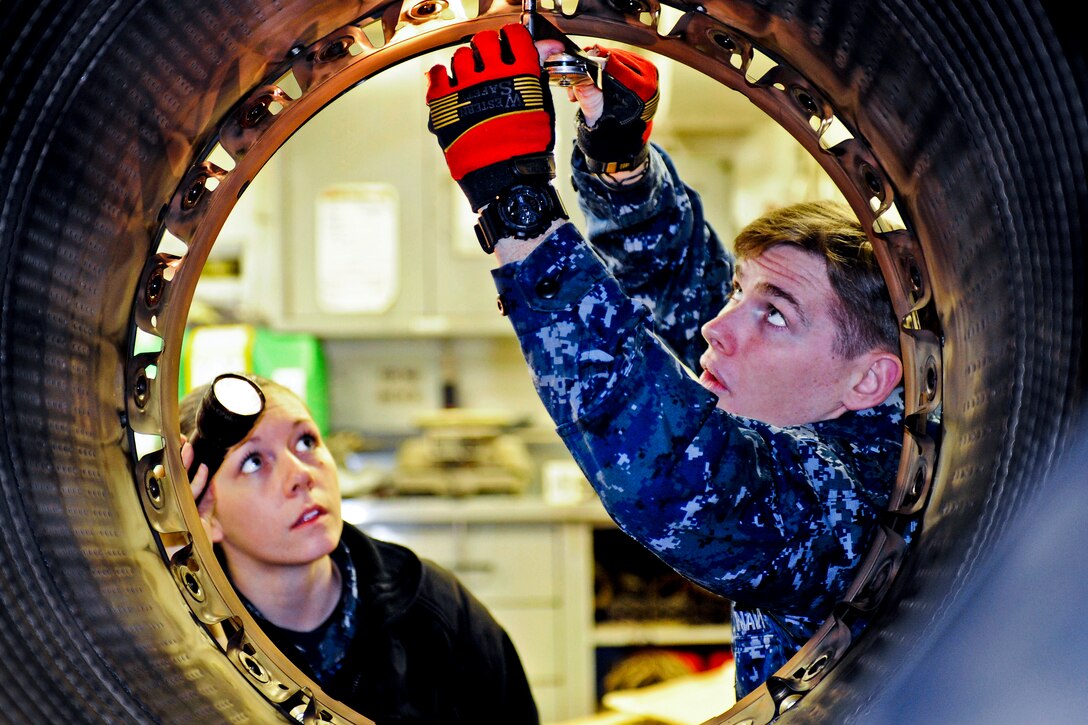 Navy Seamans Michael Walsh, right, and Chandra Tremayne perform maintenance on a 404-400 jet engine afterburner aboard the aircraft carrier USS Nimitz in Everett, Wash., March 19, 2012. Walsh and Tremayne are aviation machinist's mates airmen. The engine components will be used on an F-18 Legacy aircraft. Nimitz recently arrived at its new homeport of Everett.  
