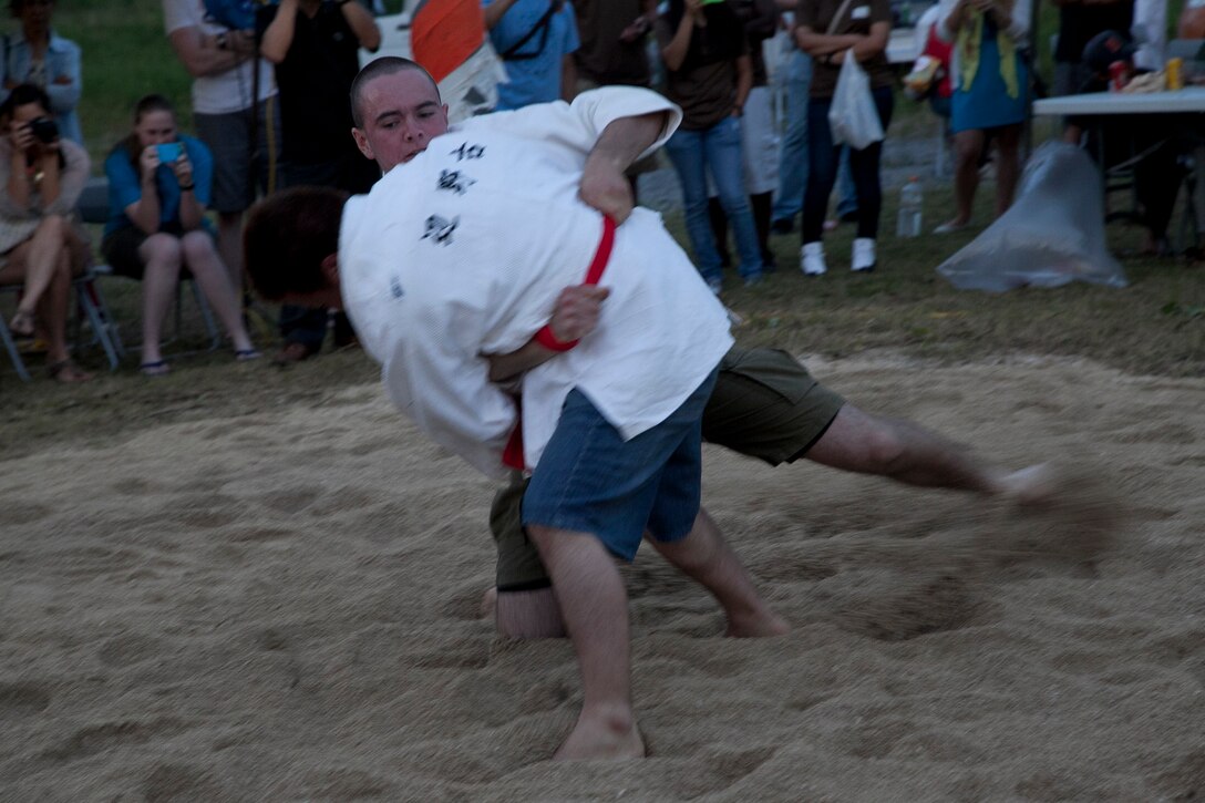 Lance Cpl. Tom M. Enright, center rear, unsettles the footing of Yoshiya Sakumoto May 31 during the annual Henoko Okinawa-Style Sumo Tournament at Mae-No-Hama field in Henoko. During a bout, a competitor tries to earn points by making the opponent to fall into the “dohyo,” or sandy pit, without striking or letting go of each other’s belts. The first to gain two points is the winner. Enright is a Deadwood, S.D., native and electro-optical ordnance repairer with Combat Assault Battalion, 3rd Marine Division, III Marine Expeditionary Force. (U.S. Marine Corps photo by Lance Cpl. David N. Hersey/Released)