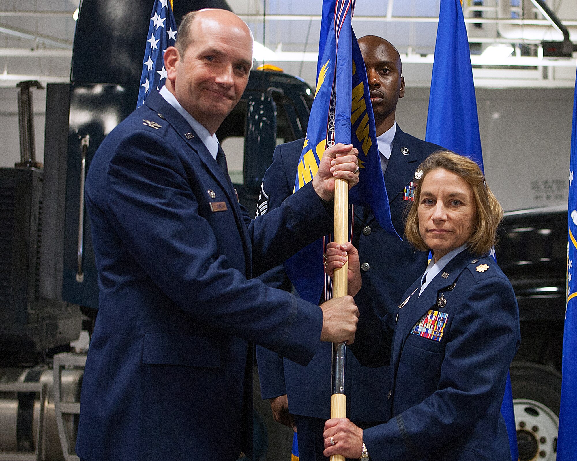 Col. Trevor Flint, 90th Maintenance Group commander, passes the 90th Operations Squadron guidon to Maj. Jacqueline Sartori as she assumes command of the squadron during a change-of-command ceremony in the 90th MXG high-bay maintenance hangar on F.E. Warren Air Force Base, Wyo., June 2, 2014. Master Sgt. Christopher Stokes, 90th MOS first sergeant, stands by to take the guidon back from Sartori. (U.S. Air Force photo by R.J. Oriez)