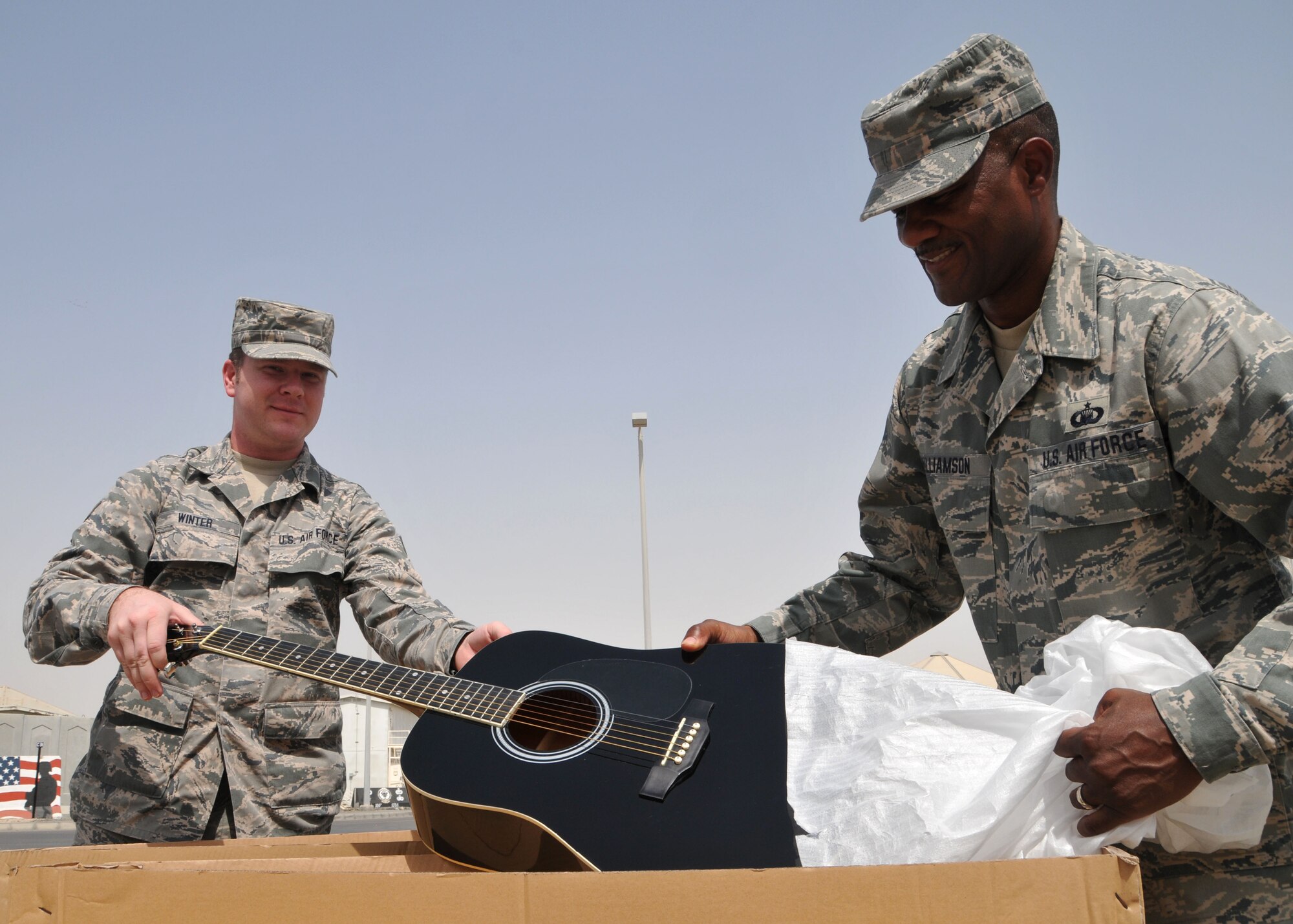 Air Force Senior Airman Erik Winter and Air Force Master Sgt. Andre Williamson, both chaplain assistants, unpack one of the donated guitars to be used by Airmen assigned to the 380th Air Expeditionary Wing at the undisclosed location in Southwest Asia June 4, 2014. (U.S. Air Force photo by Senior Master Sgt. Eric Peterson/Released)