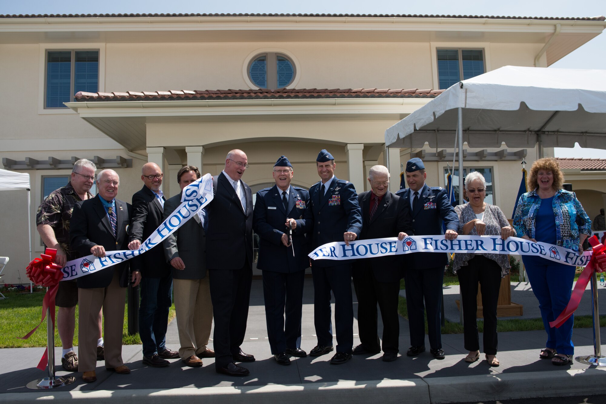 Brig. Gen. Charles Potter, center, Air Force assistant surgeon general, cuts a ribbon to formally open Fisher House II May 30 at Travis. Base leaders, Fisher House organizers and numerous distinguished visitors from the community celebrated the oepning of the home that will provide a place of comfort for military members, veterans and their families who are enduring health-related hardships. (U.S. Air Force photo/Ken Wright)
