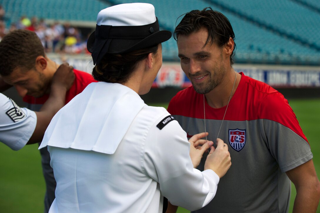 Navy Petty Officer 2nd Class Autumn Devine places a custom dog tag around the neck of Chris Wondolowski, forward player on the U.S. Men's National Soccer Team, during a ceremony at Everbank Stadium, Jacksonville, Fla., June 6, 2014.