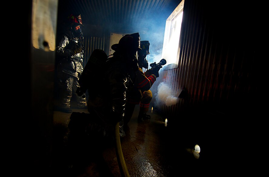 Firefighters from the 5th Civil Engineer Squadron participate in a controlled burn exercise at Minot Air Force Base, N.D., May 21, 2014. The multi-use structure provides an ability to train firefighters at all levels, from hose evolutions to command and control scenarios. It has movable walls to change room layout, and can test firefighter skills conducting search patterns and victim locating in blackout conditions. It provides opportunity for forcible entry training, confined space rescue, and offers realistic and scenario based sounds during training to add to the realism. (U.S. Air Force photo/Senior Airman Brittany Y. Bateman)