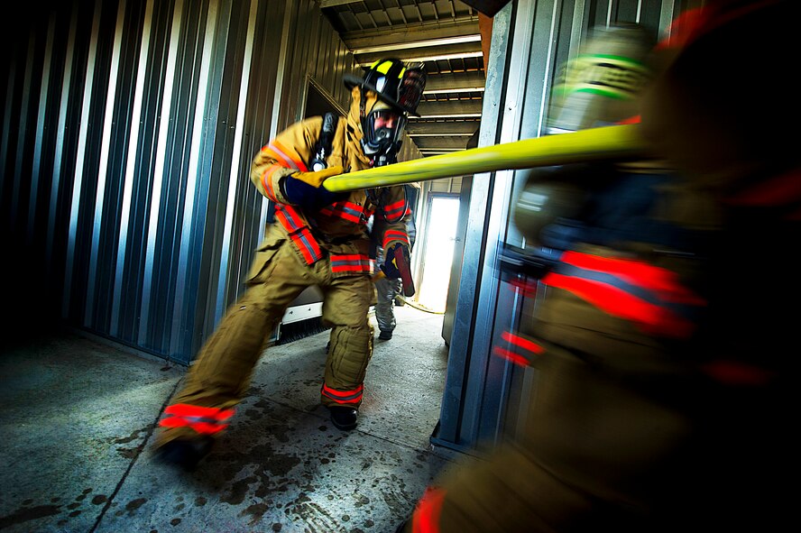 Firefighters from the 5th Civil Engineer Squadron participate in a controlled burn exercise at Minot Air Force Base, N.D., May 21, 2014. The multi-use structure provides an ability to train firefighters at all levels, from hose evolutions to command and control scenarios. It has movable walls to change room layout and can test firefighter skills conducting search patterns and victim locating in blackout conditions. It provides opportunity for forcible entry training, confined space rescue, and offers realistic and scenario based sounds during training to add to the realism. (U.S. Air Force photo/Senior Airman Brittany Y. Bateman)