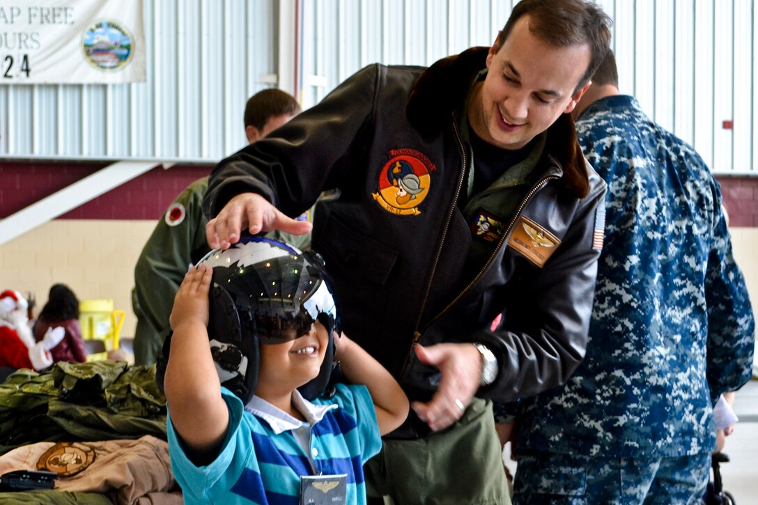 Navy Lt. Cmdr. Jeremy Fischer helps a child put on a flight helmet during the annual Make-A-Wish Foundation children's holiday visit on Naval Air Station North Island, Calif., Dec. 3, 2011. Fischer is assigned to Logistics Support Squadron 57, which hosts the annual event to give children an inside look at life in the military.  
