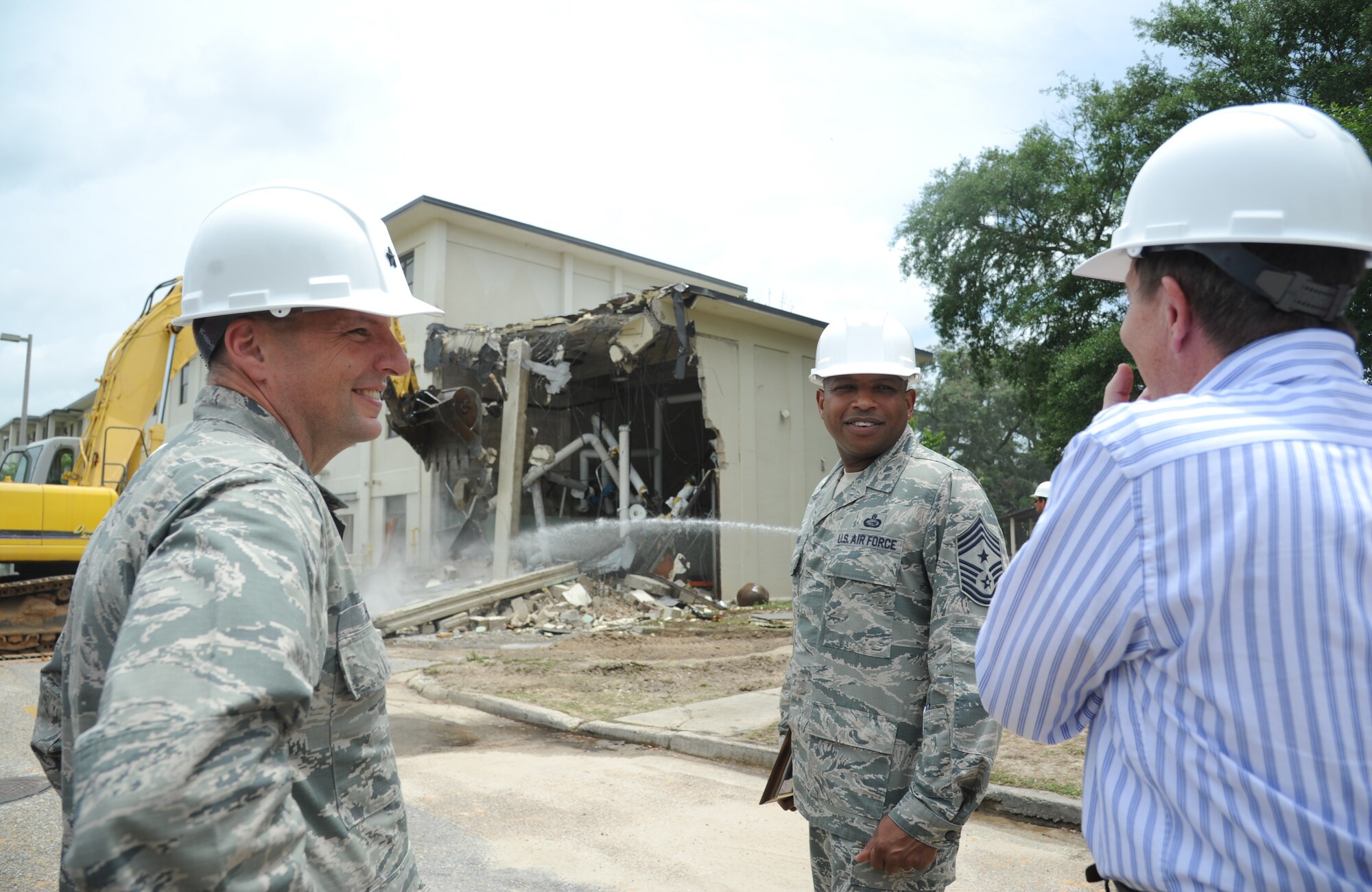 Brig. Gen. Patrick Higby, 81st Training Wing commander, and Chief Master Sgt. Farrell Thomas, 81st TRW command chief, speak with Don Kinman, Base Operations Support contractor, as the demolishing of building 4815 takes place in the background June 10, 2014, at Keesler Air Force Base, Miss.  The demolishing of Building 4815 was started by Higby and Thomas and will be continued by Business Integrity Commission, the prime demolishing contractor, as well as building 4813. (U.S. Air Force photo by Kemberly Groue)